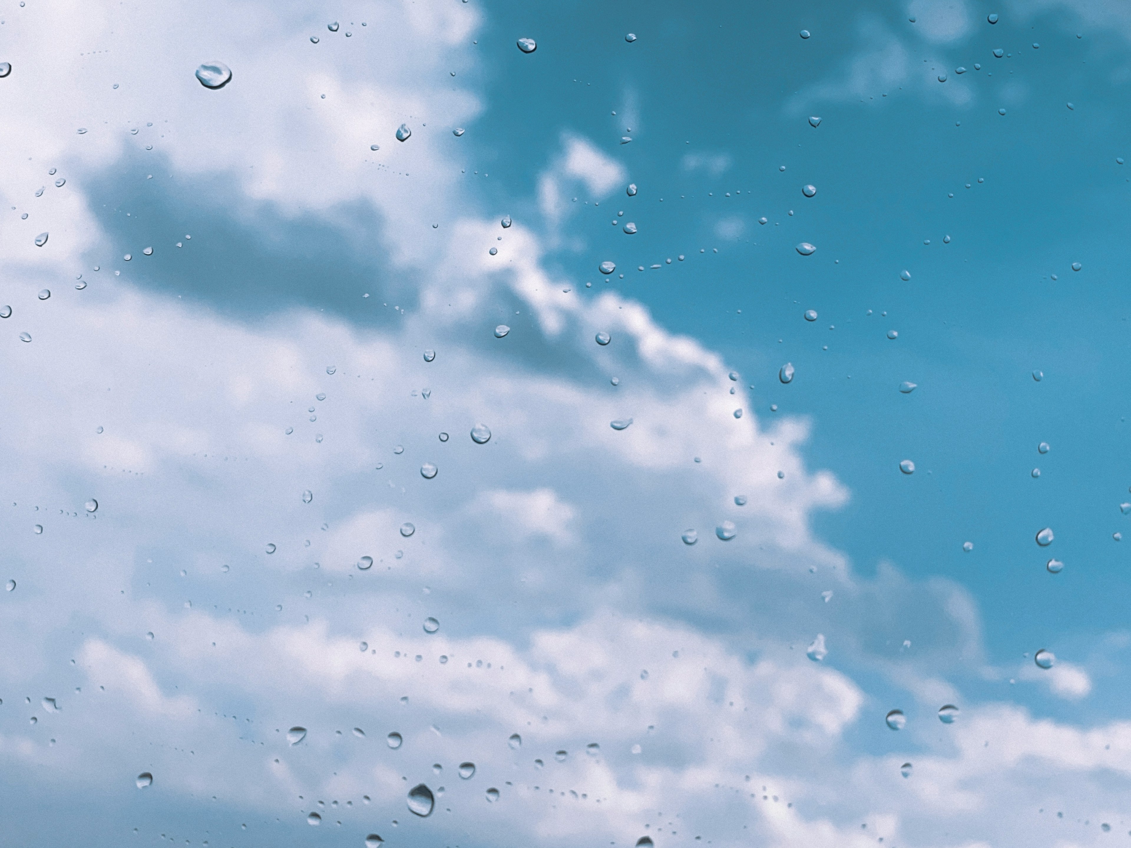 青空と雲を背景にした雨滴のある窓