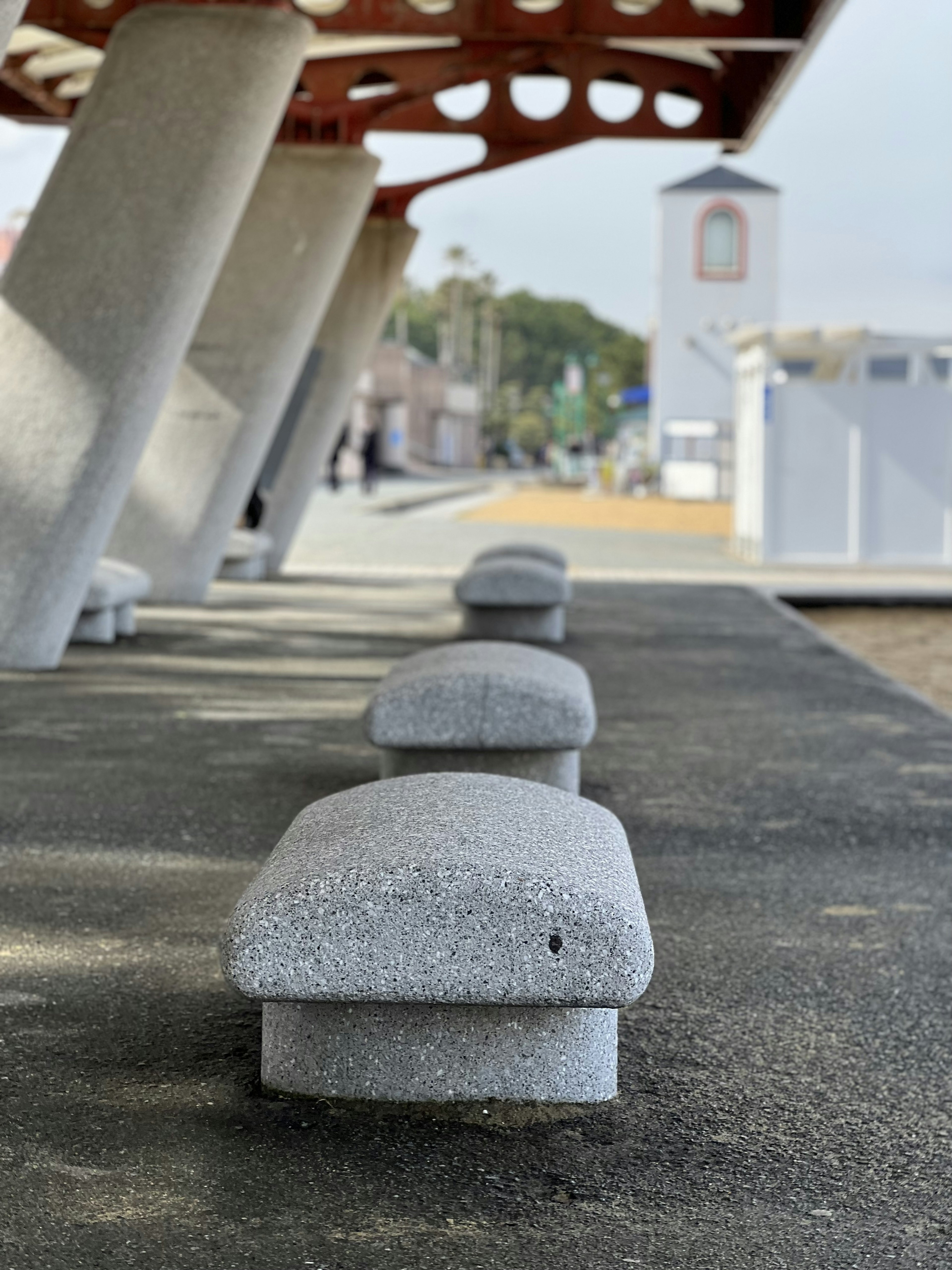 Gray concrete benches lined along a paved walkway with a red-roofed structure