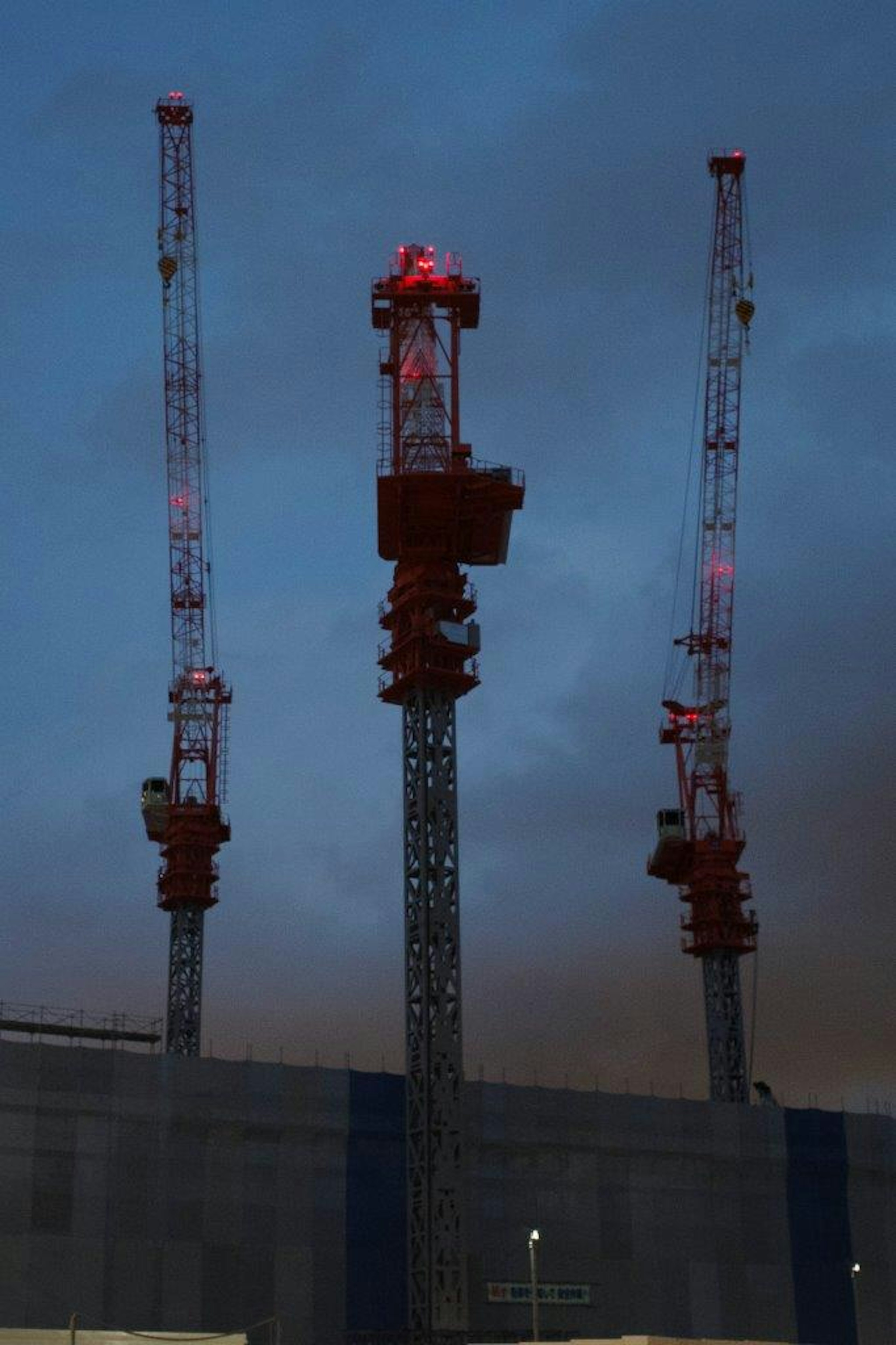 Tiga crane dengan lampu merah berkedip di langit malam