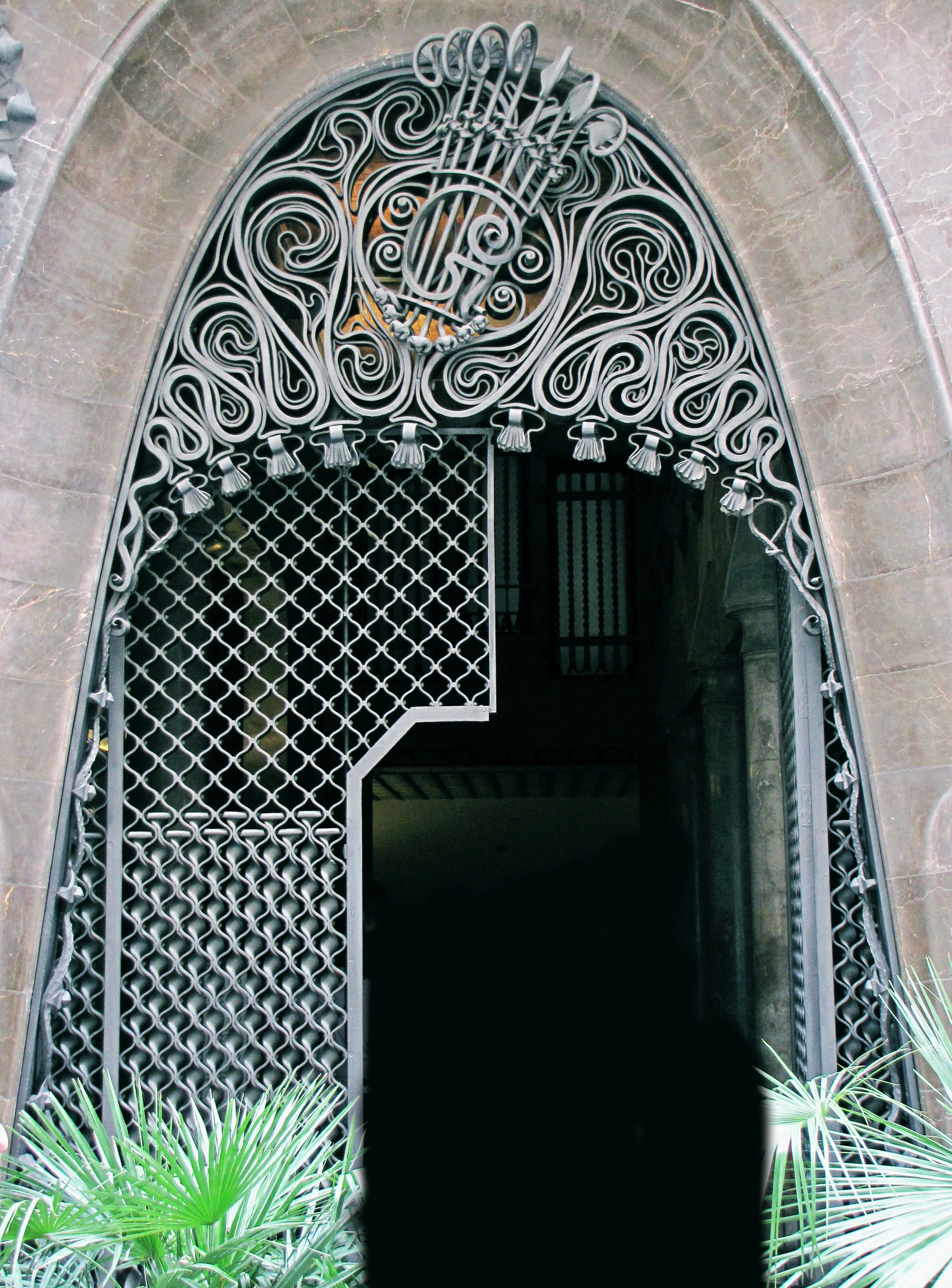 Arched metal door with intricate decorative patterns and greenery