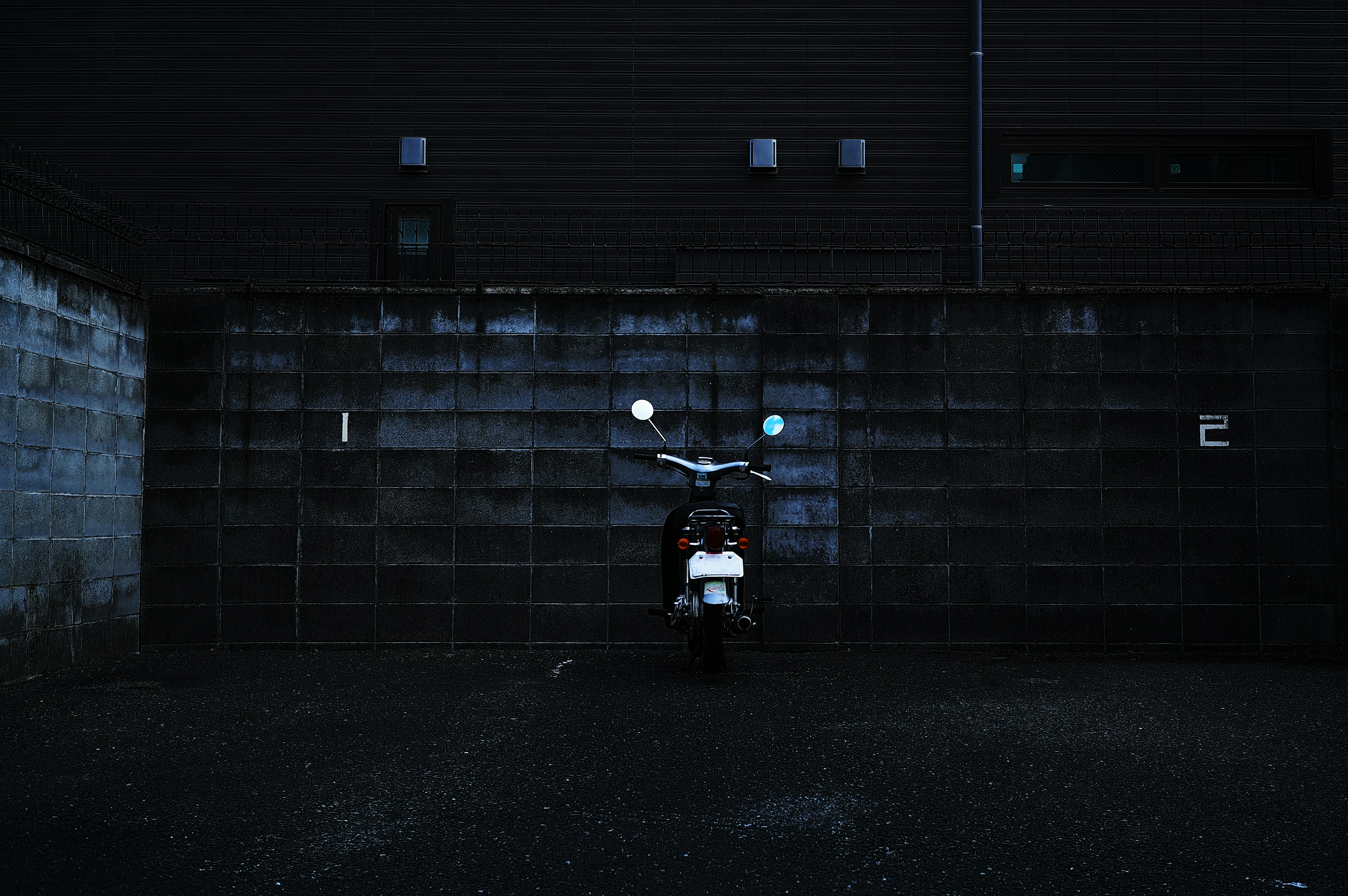 Moto blanche garée contre un mur en béton sombre avec des chiffres