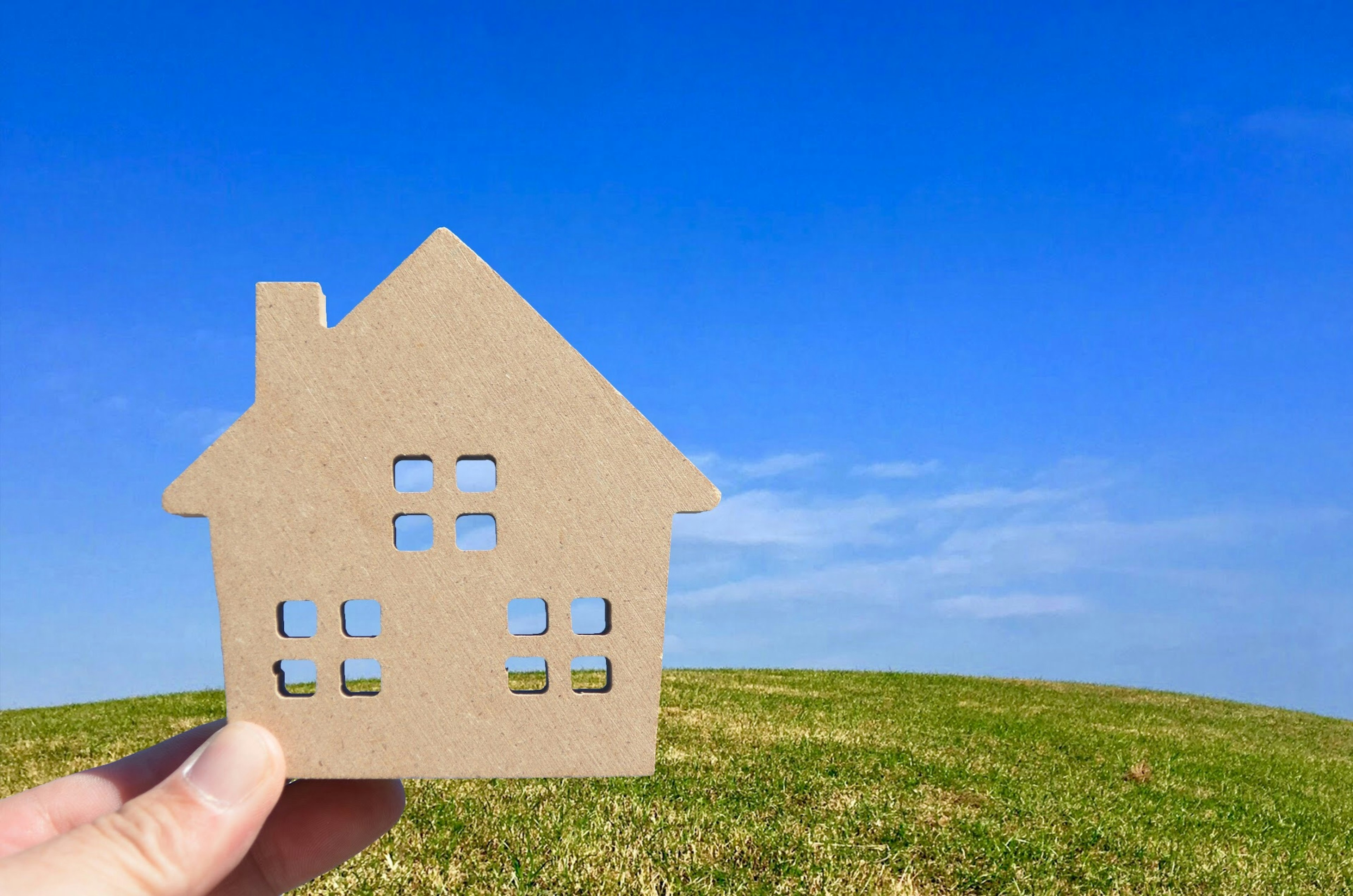 Un modello di casa di cartone tenuto in mano sotto un cielo azzurro