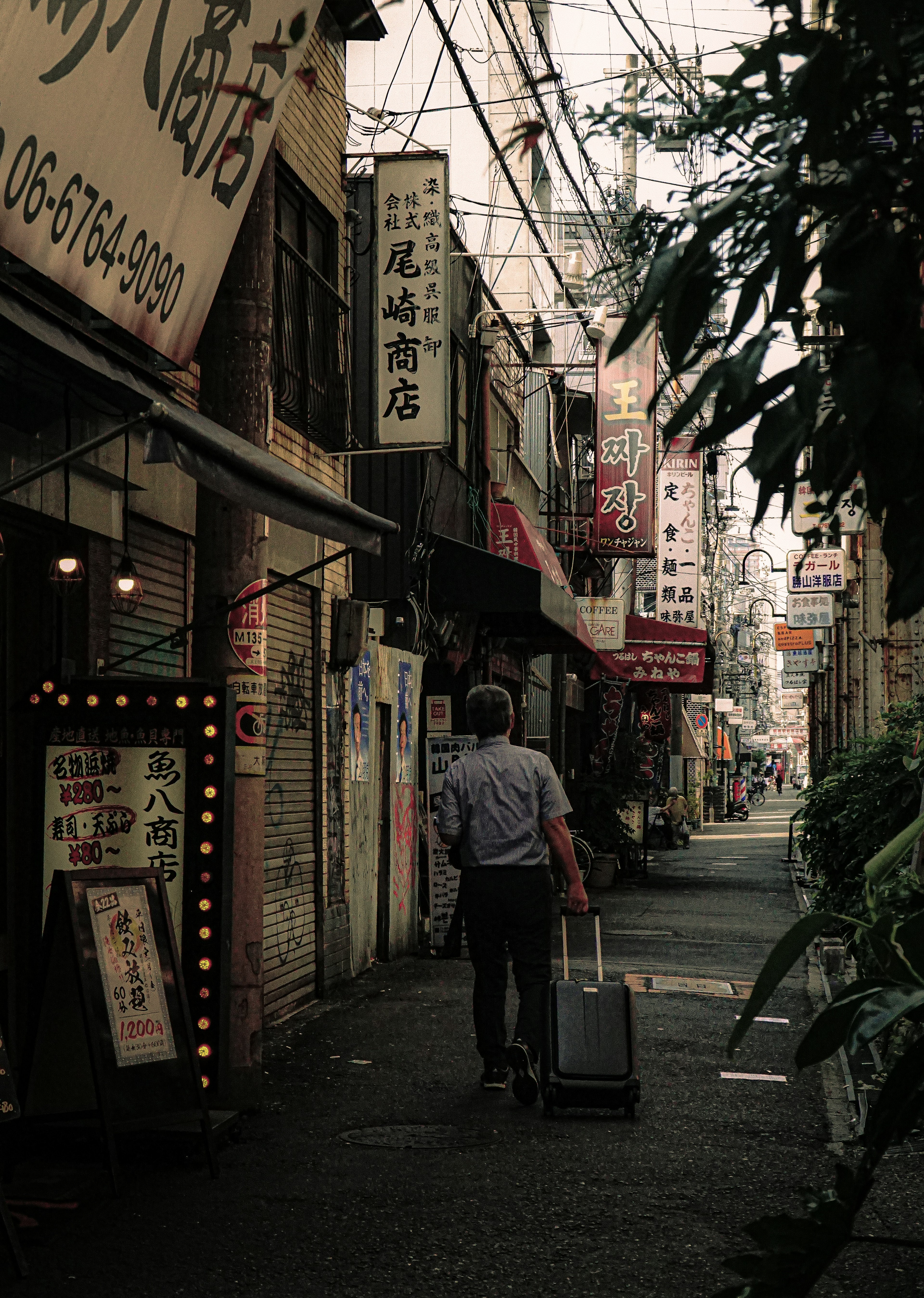 Man walking in a narrow alley with a suitcase surrounded by restaurant signs