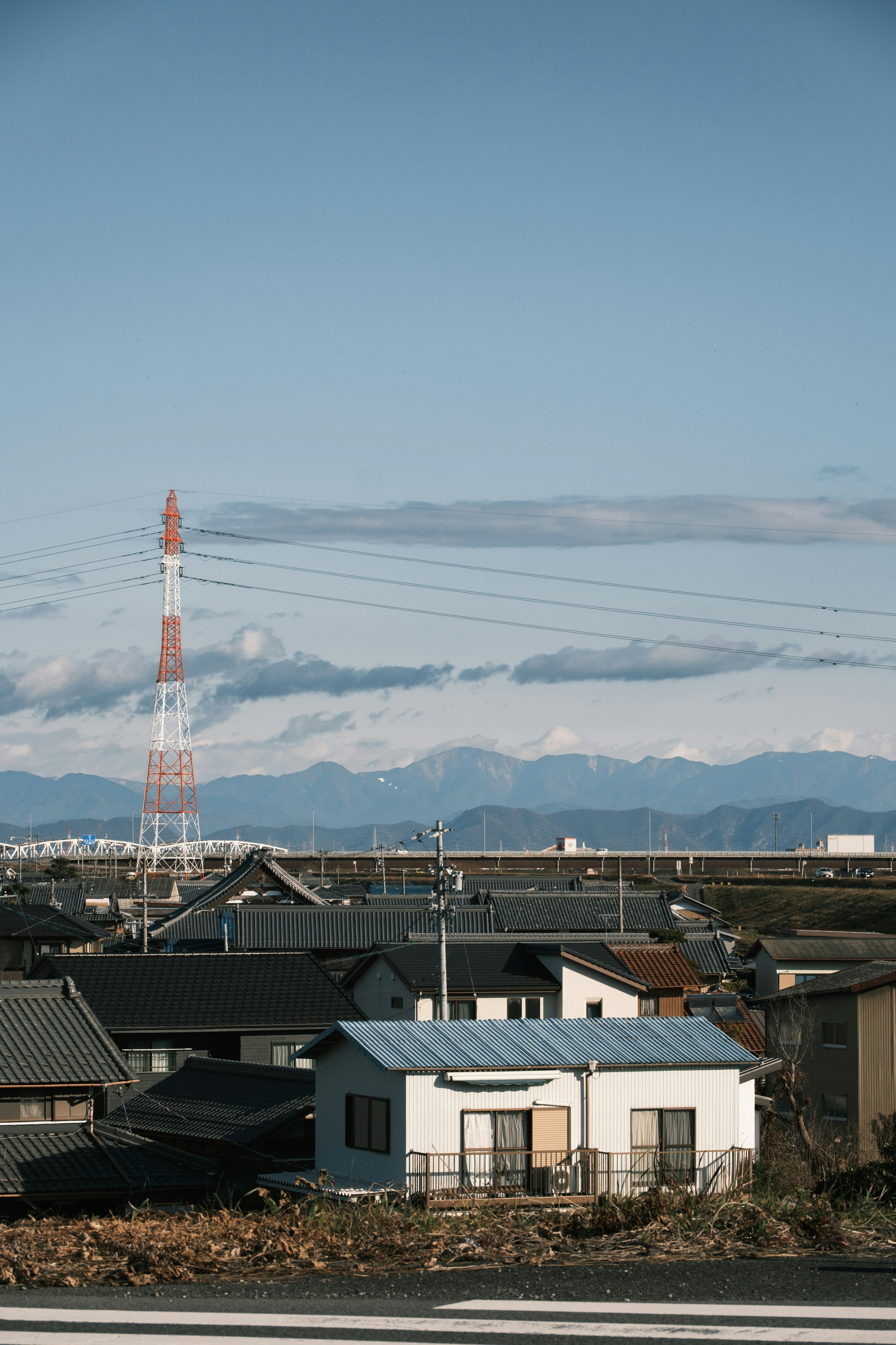 青い空と山々の背景に白い家と赤い電波塔がある風景