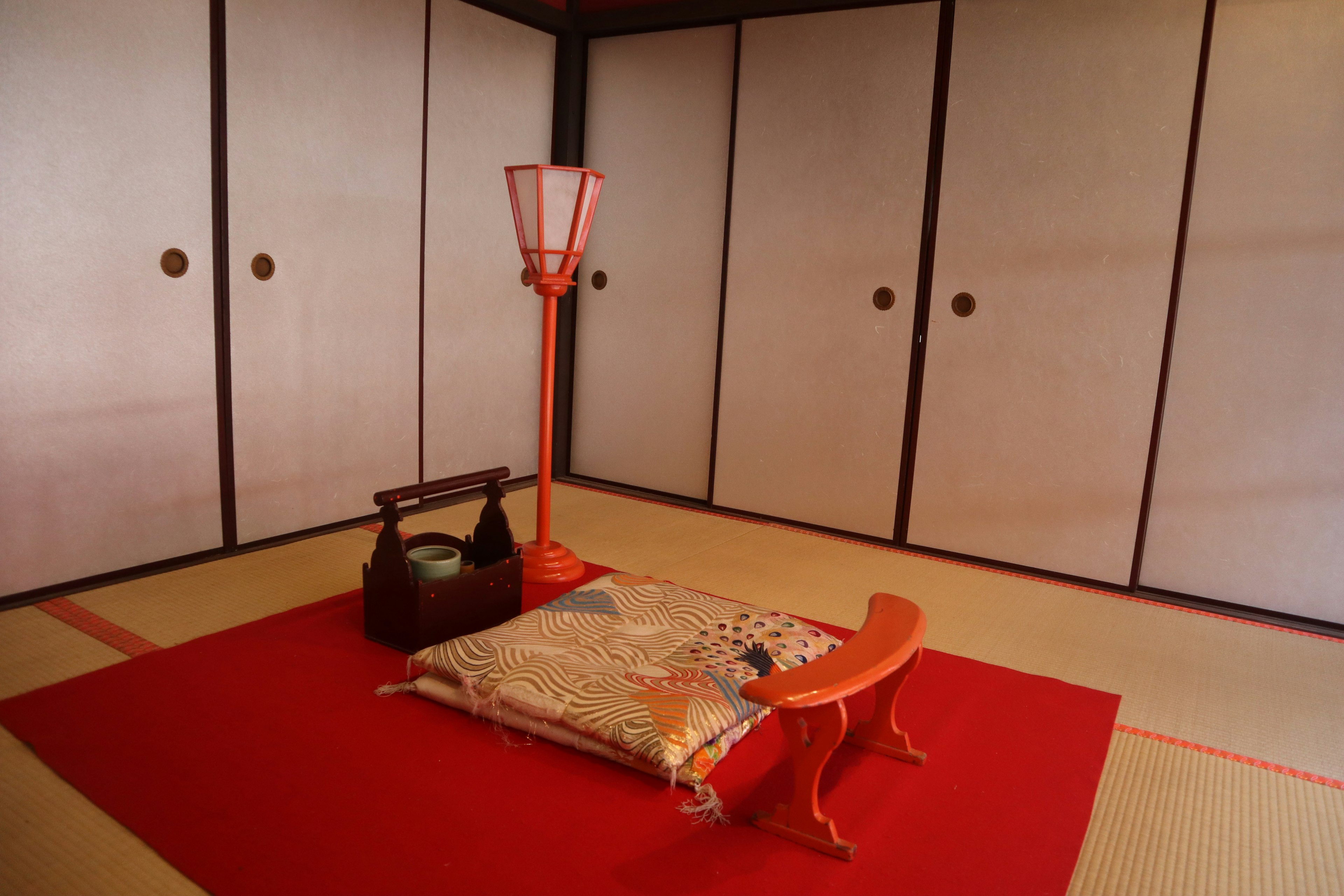 Interior of a Japanese room with a red carpet and a cushion featuring an orange lamp and a black tea set