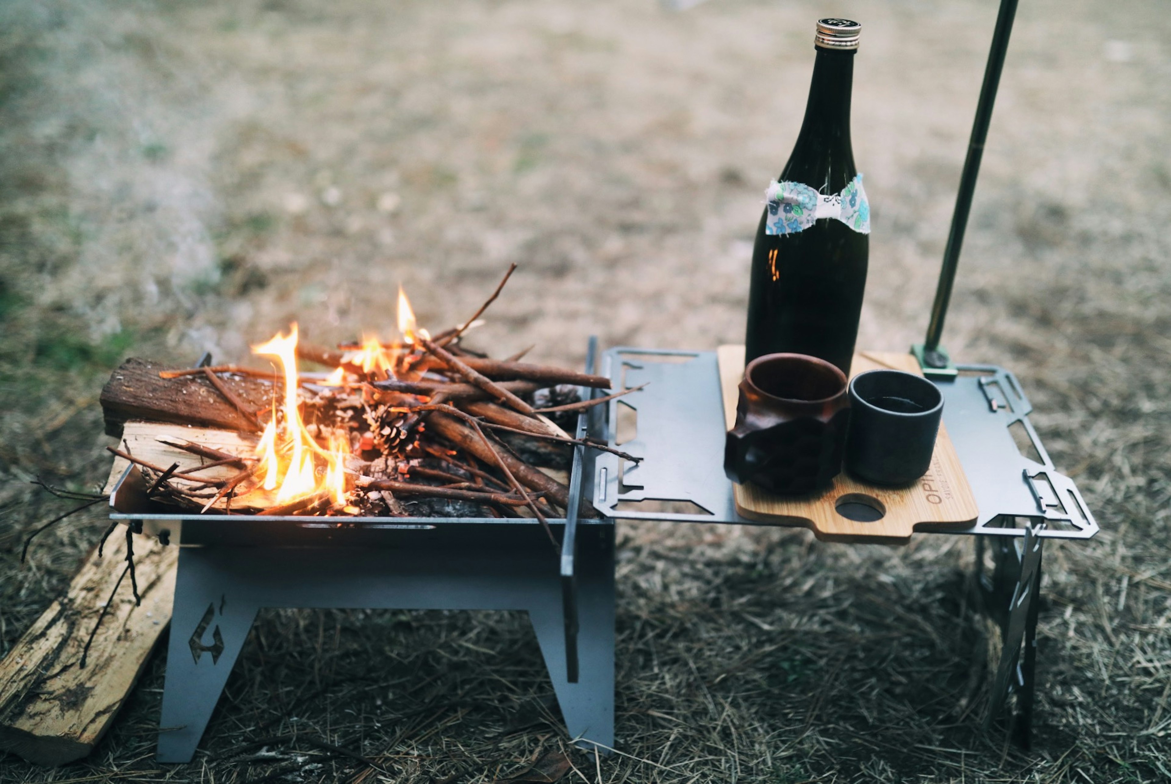 Ein Lagerfeuer mit einer Flasche Wein und Tassen auf einem tragbaren Tisch