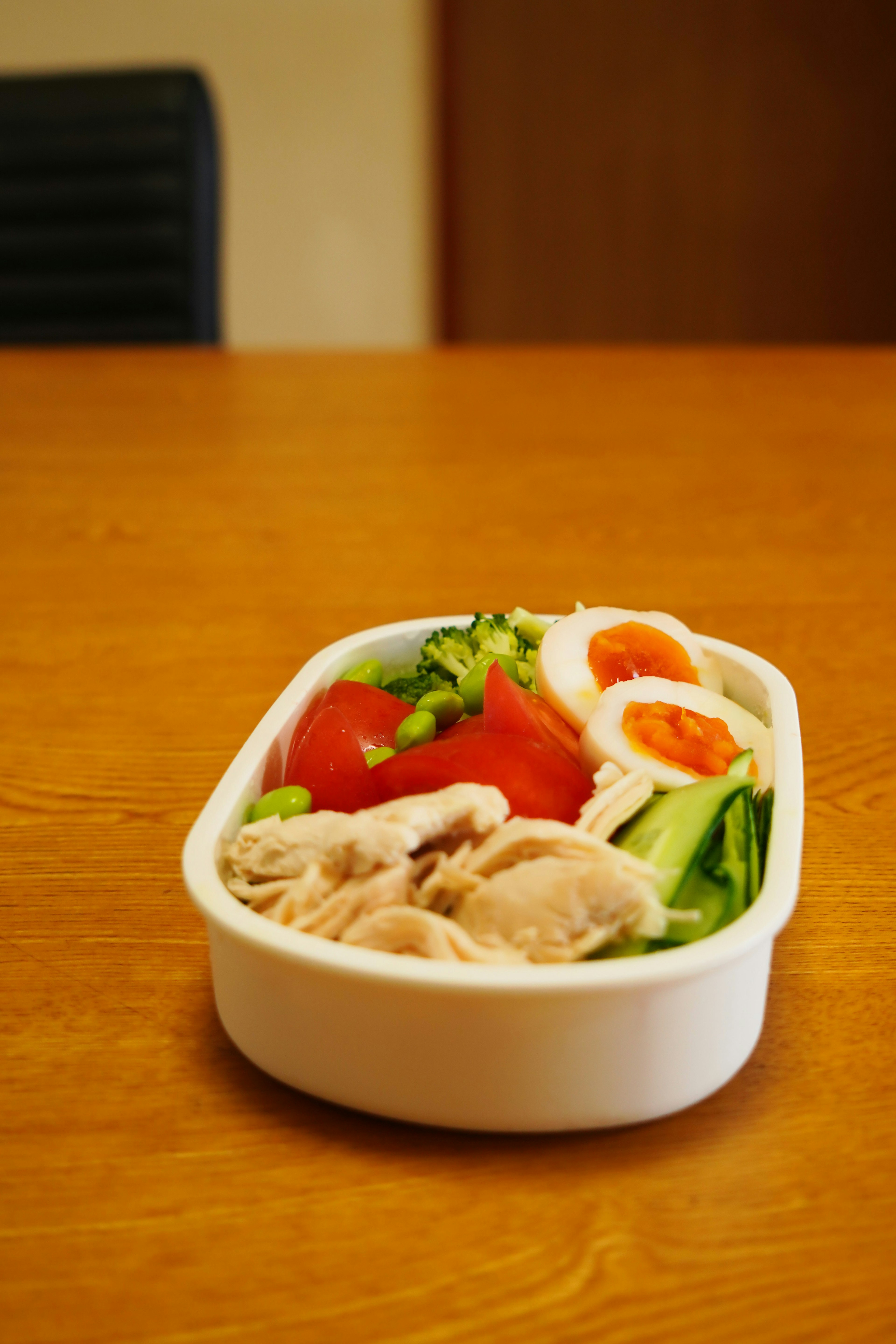 A white lunch box filled with fresh vegetables and meat dish