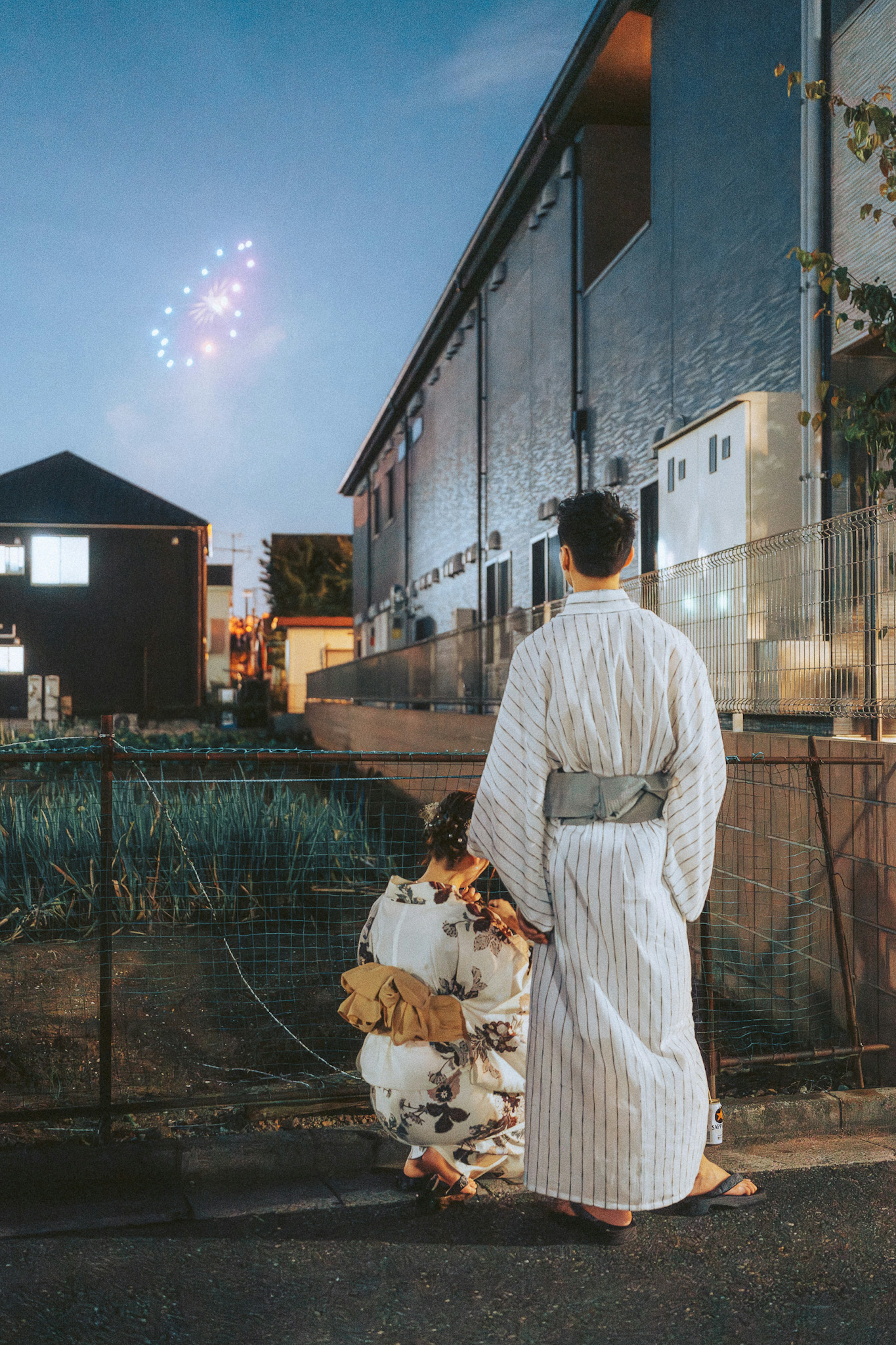 夕暮れ時に花火を見上げる二人の和服姿の男女