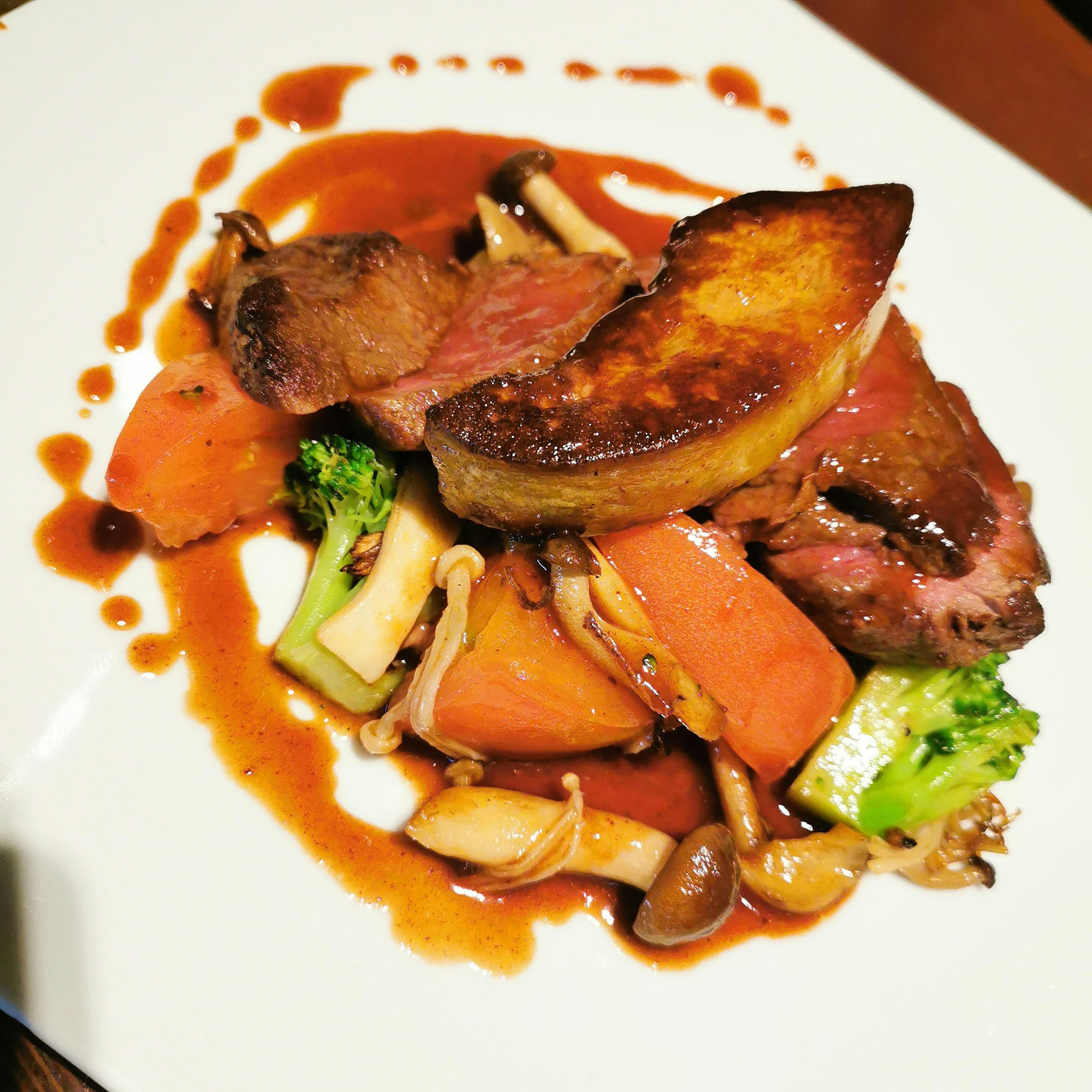 Plated meat dish featuring foie gras and assorted vegetables