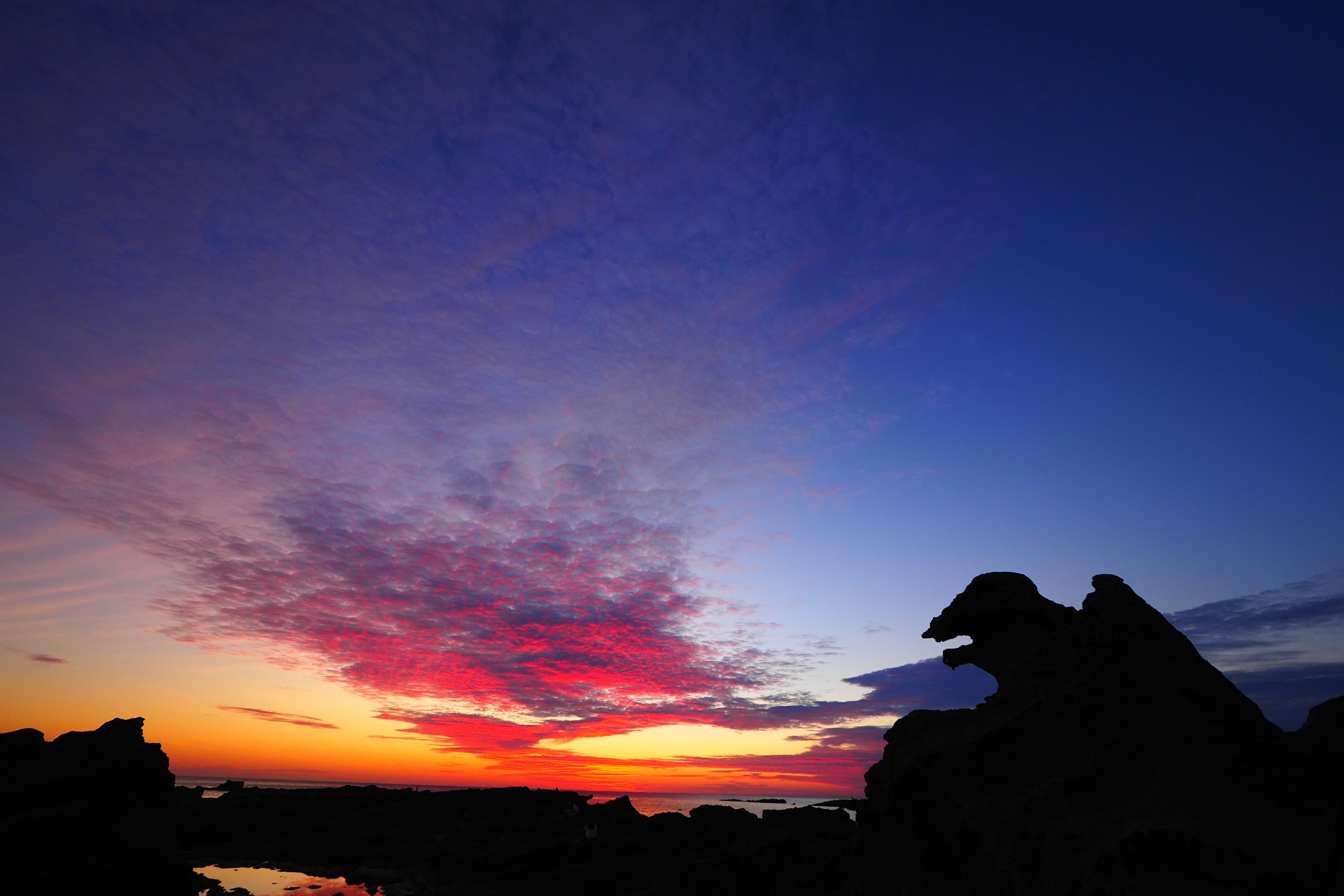 Silhouette de roches contre un ciel de coucher de soleil vibrant avec des nuages colorés