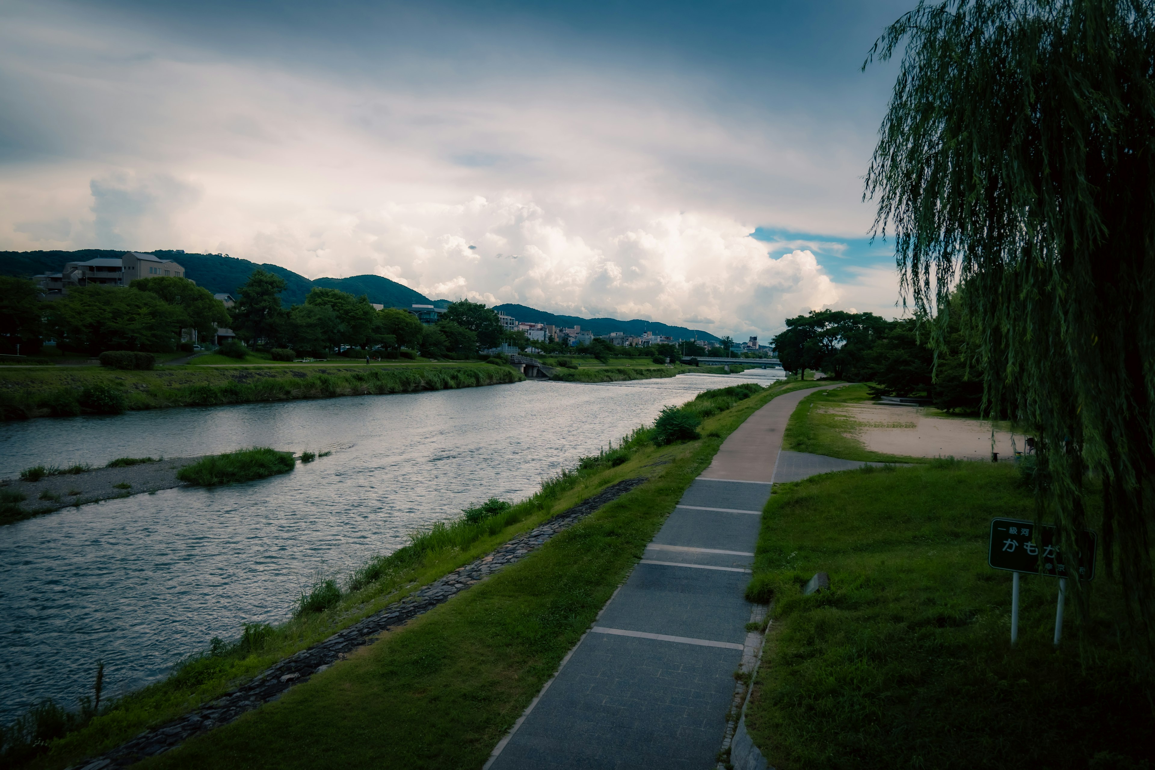 Scenic riverside path with lush greenery and dramatic clouds