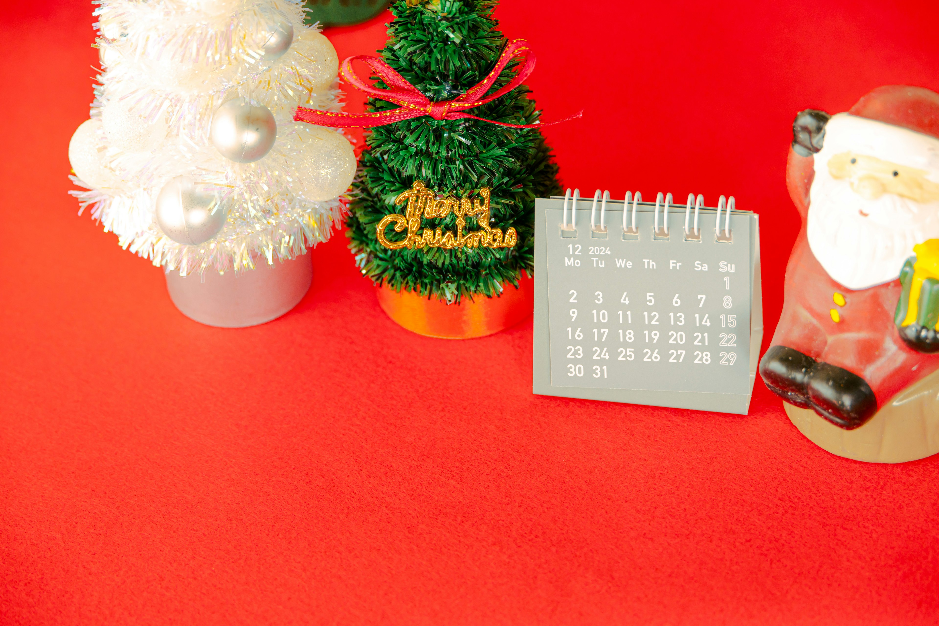 Christmas decorations including a small tree a calendar and a Santa Claus figurine on a red background