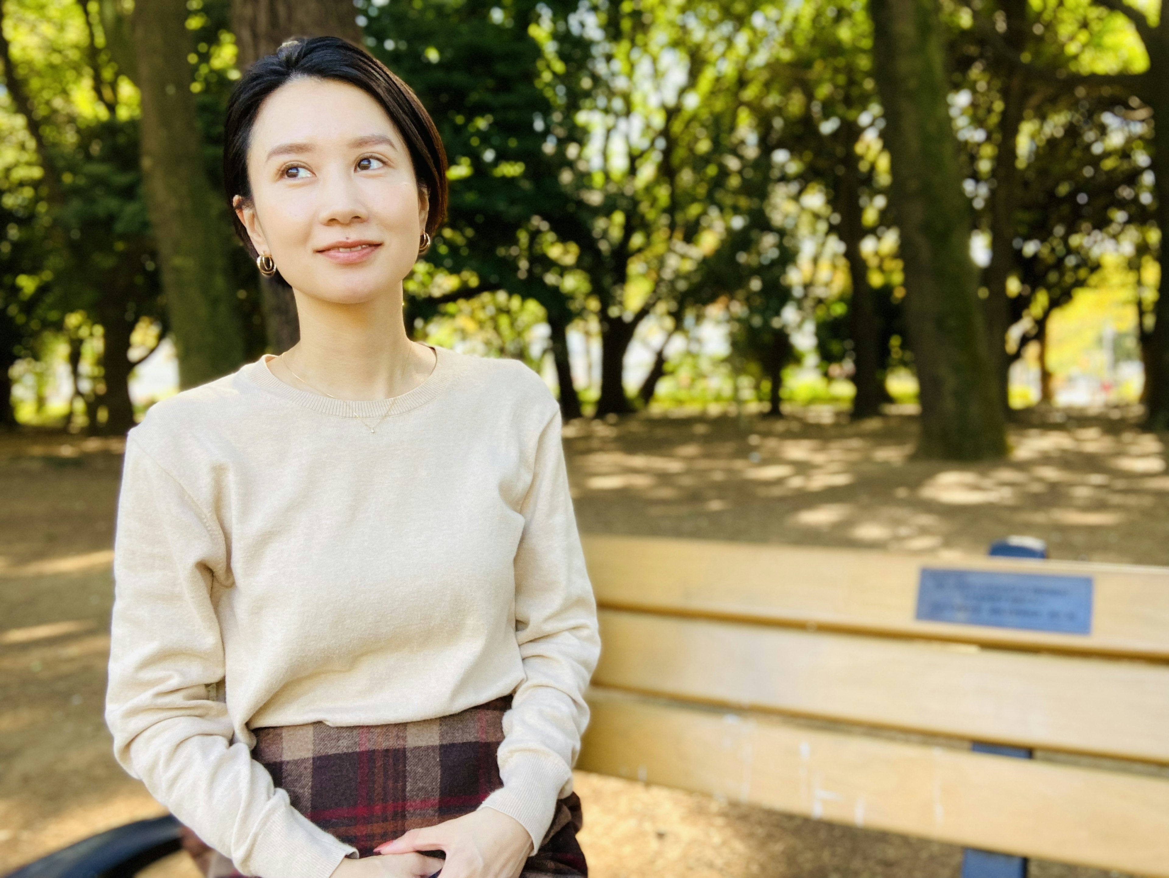 Portrait of a woman sitting on a park bench with green trees in the background and a serene expression