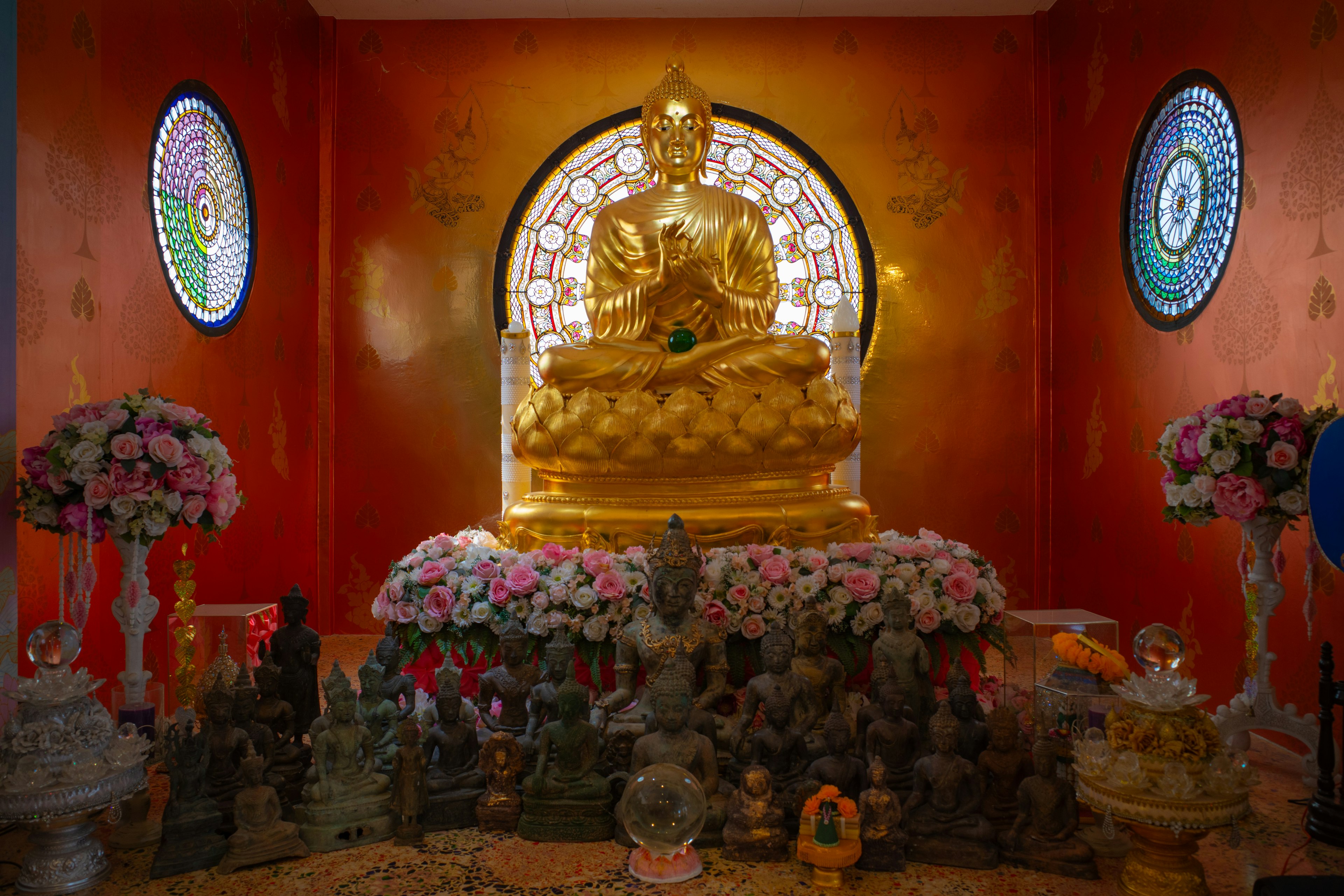 Patung Buddha emas di tengah dengan dekorasi bunga mengelilingi altar Buddha