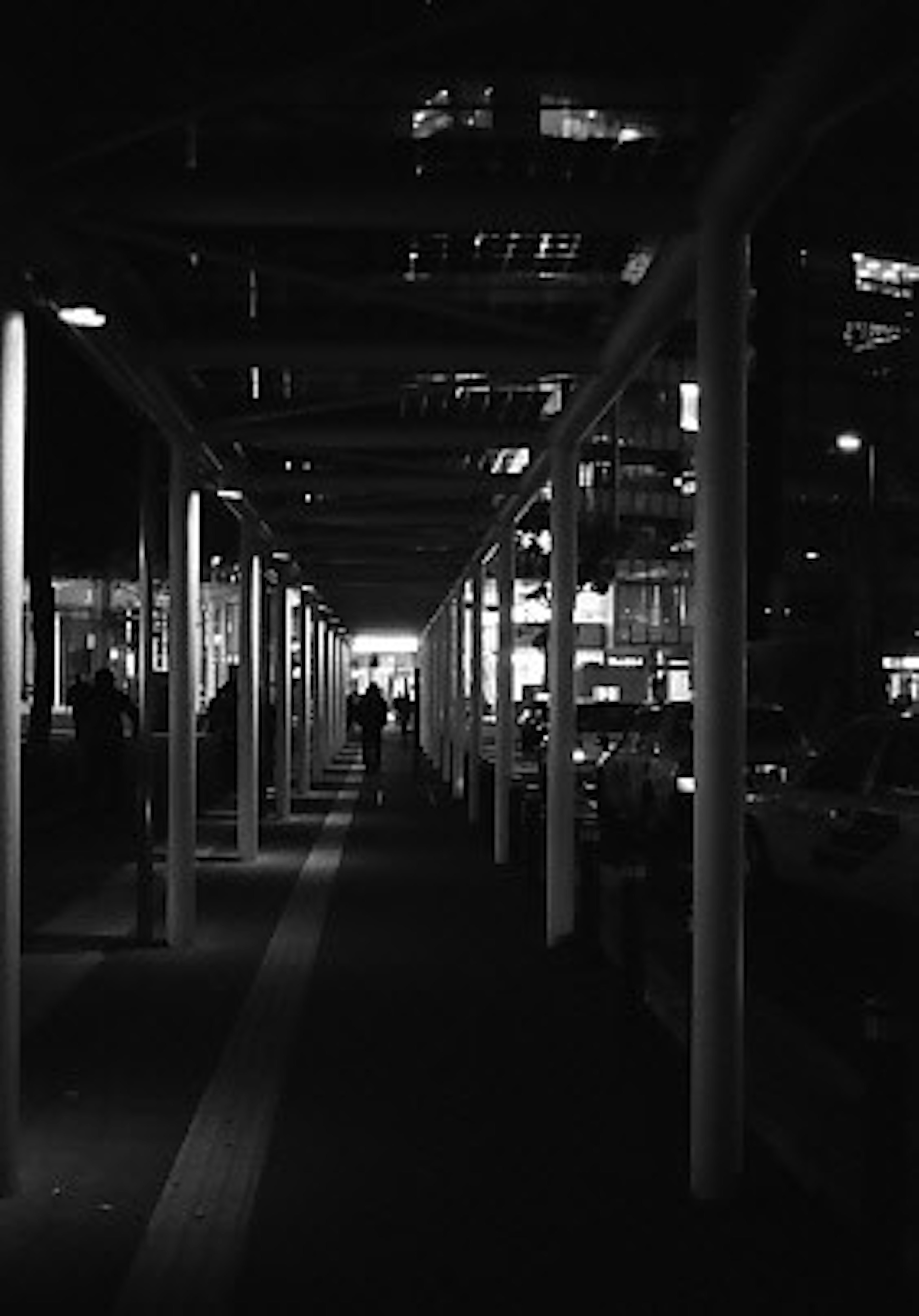 Dark walkway lined with white pillars and distant bright lights