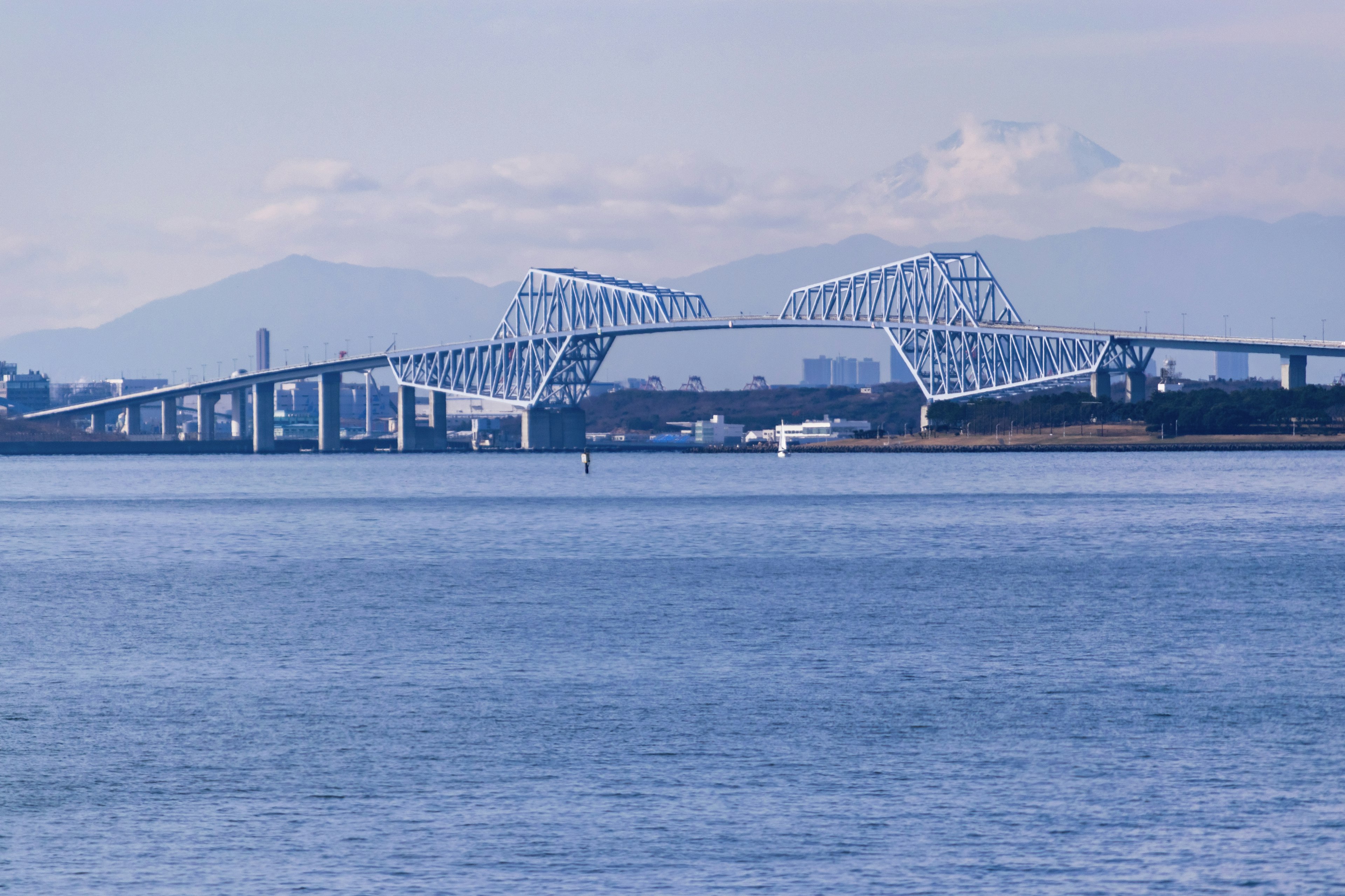 Pont au design unique reflété sur l'eau bleue avec des montagnes en arrière-plan