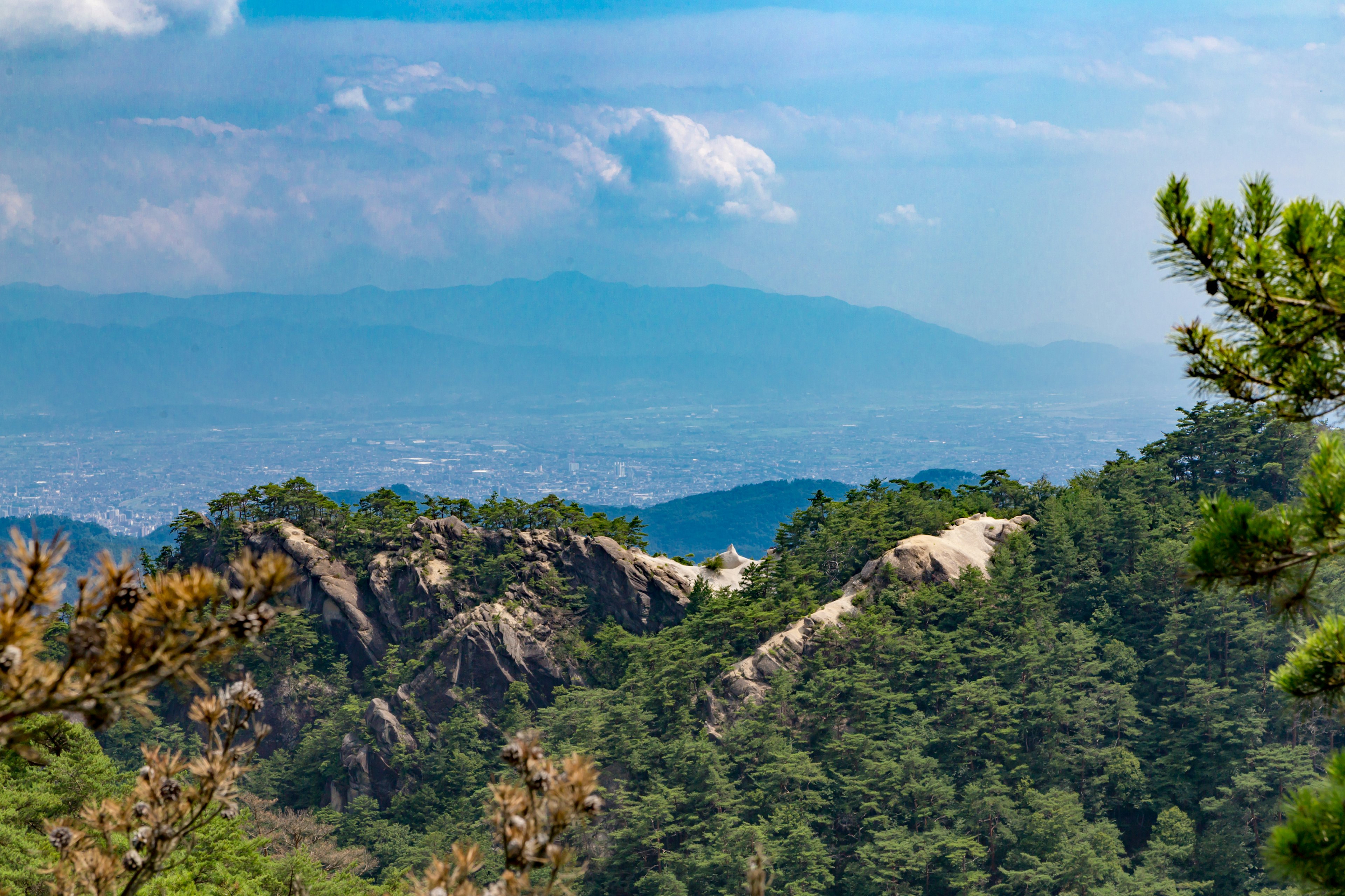 Panorama von Bergen umgeben von blauem Himmel und Wolken mit grünen Bäumen und Felsformationen