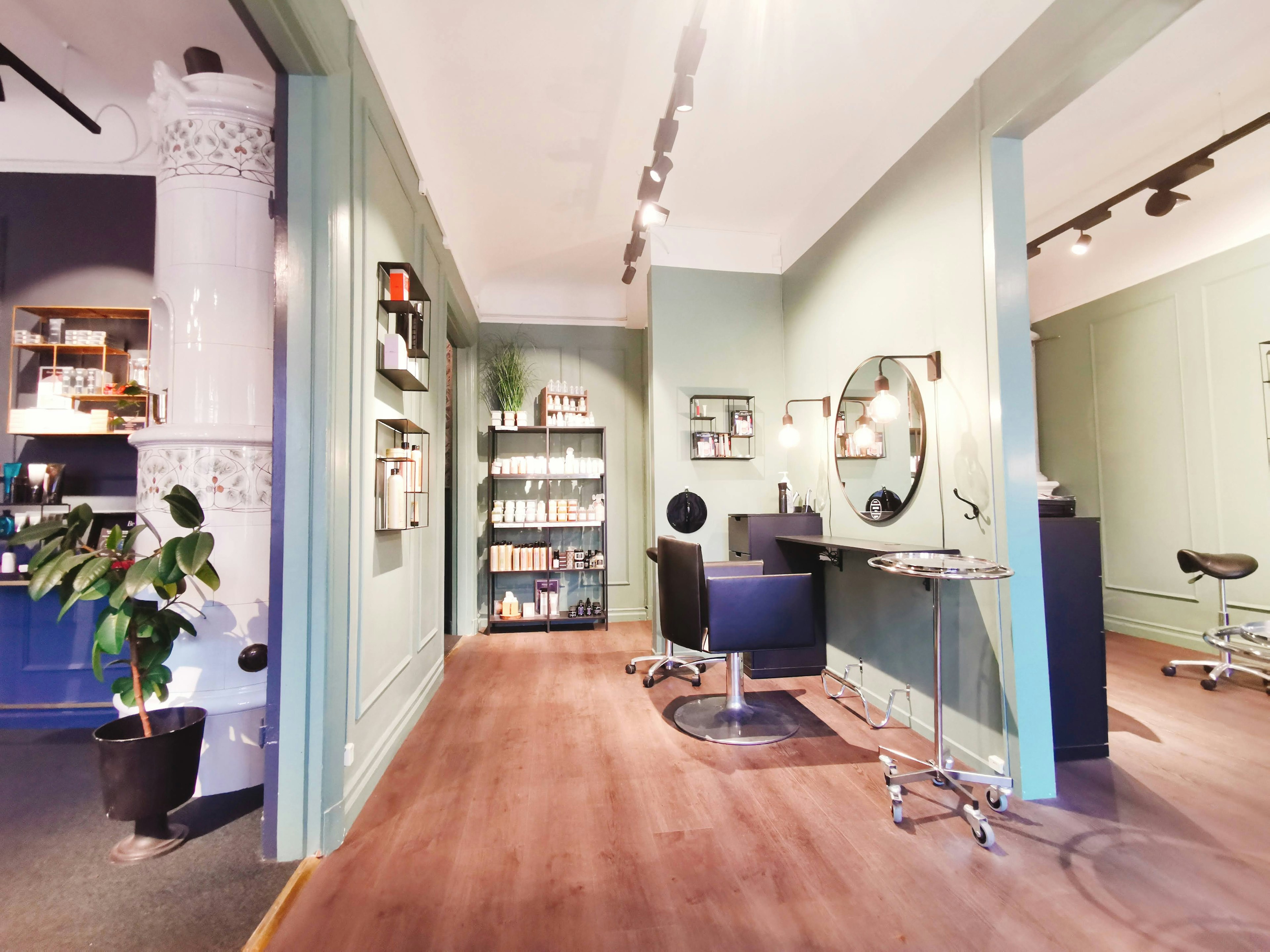 Intérieur lumineux d'un salon de coiffure avec des murs verts et un sol en bois chaises et miroirs élégants