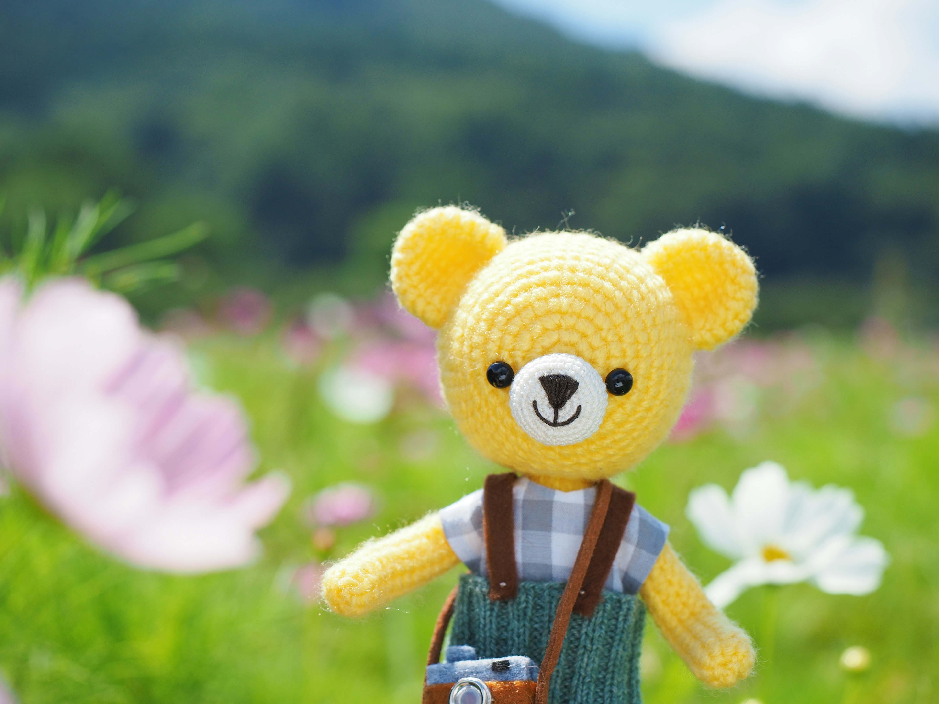 A yellow crocheted bear standing in a flower field