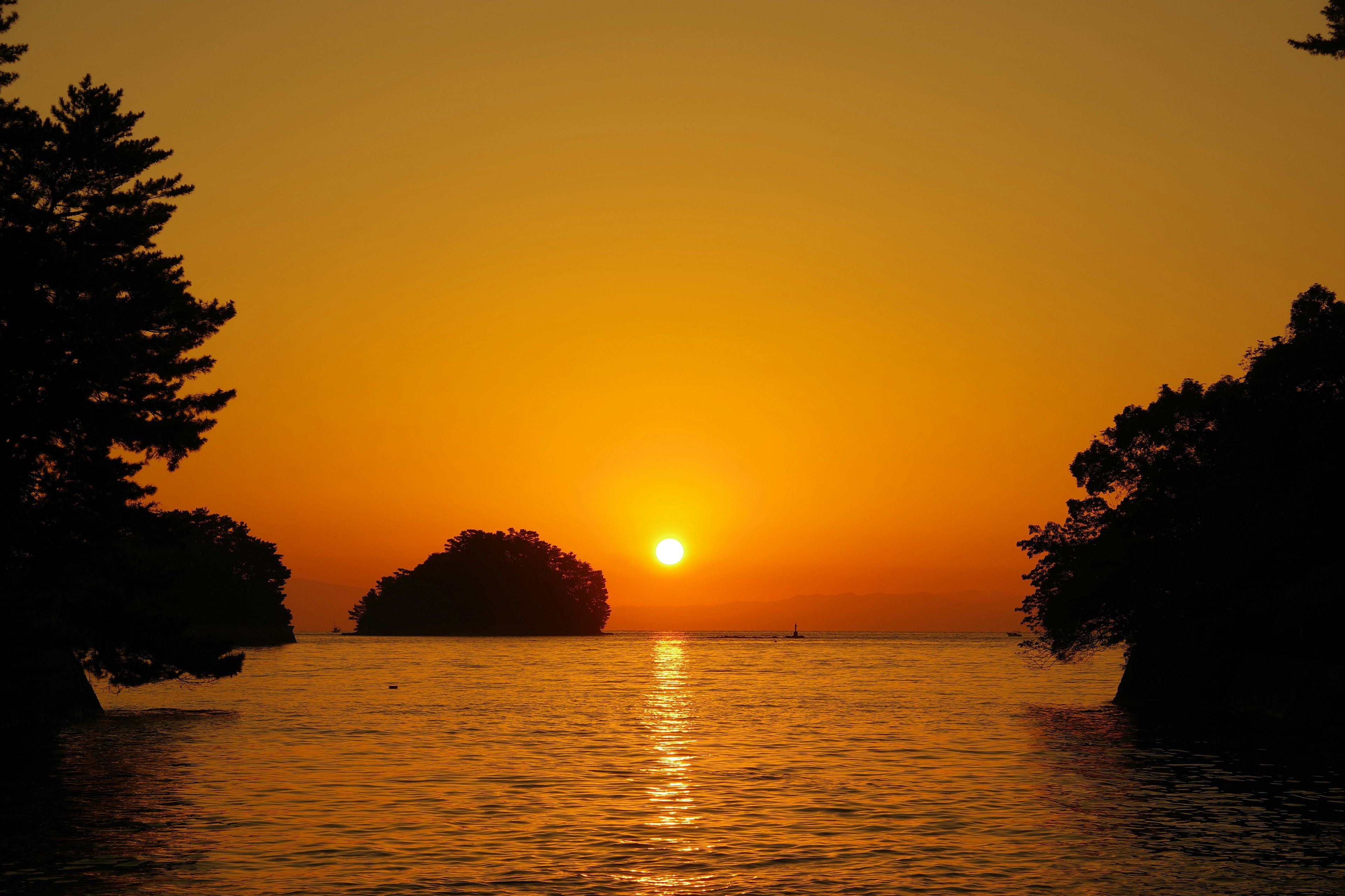 Pemandangan indah matahari terbenam di atas laut dengan air tenang dan pulau-pulau siluet