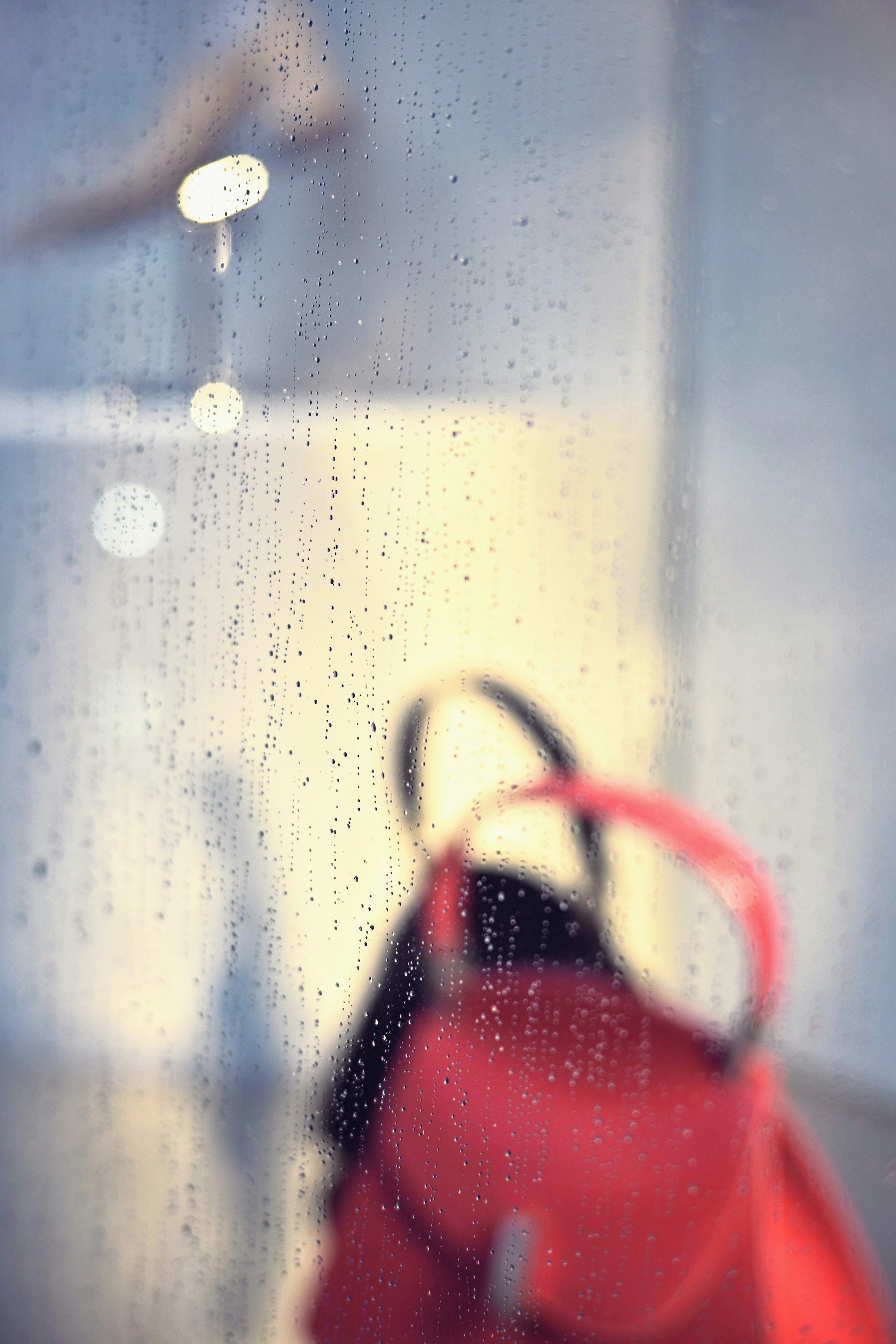 Bolso rojo borroso con un zapato al fondo detrás de un cristal salpicado de lluvia