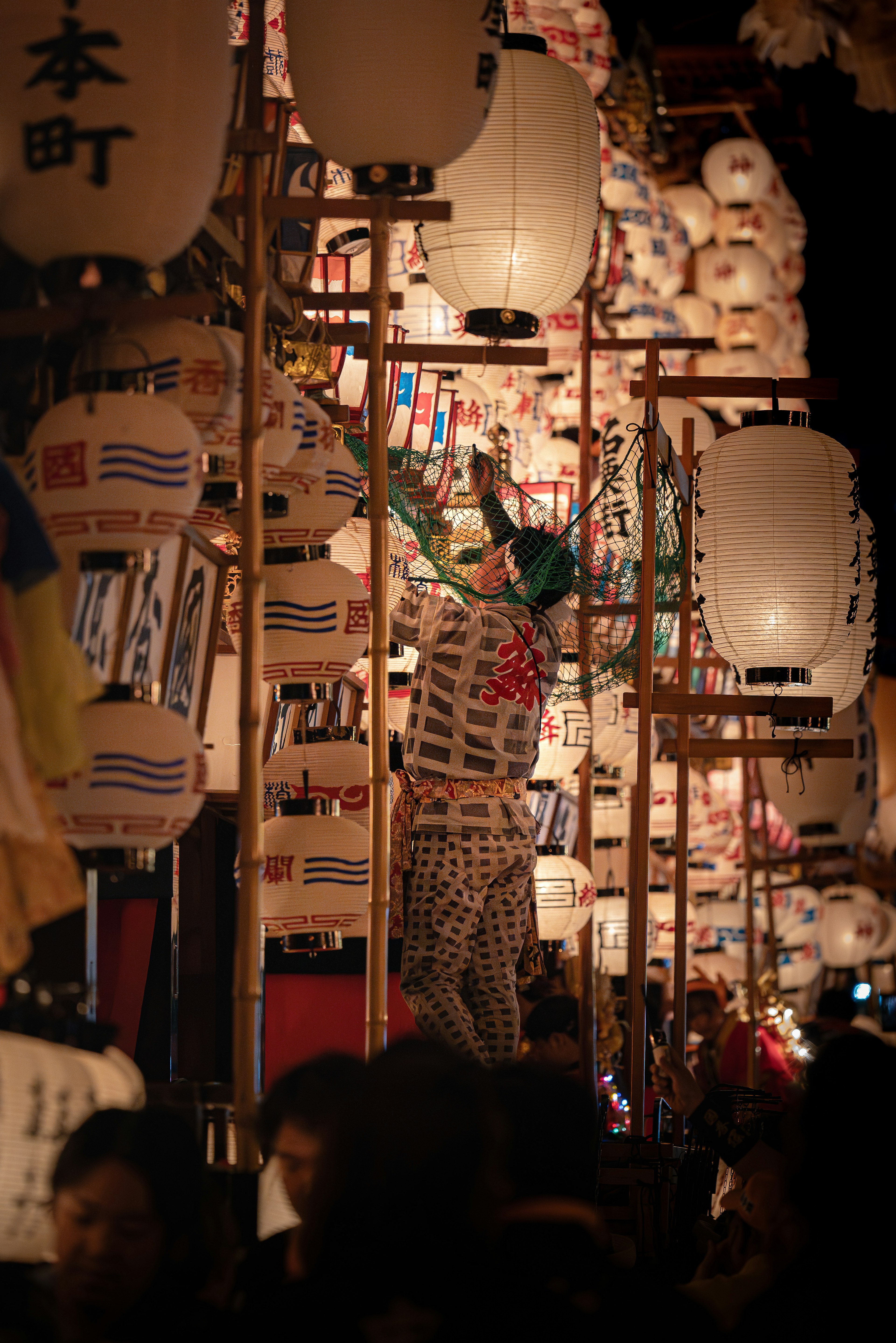 夜の祭りで提灯を取り付ける人々と賑わう通り