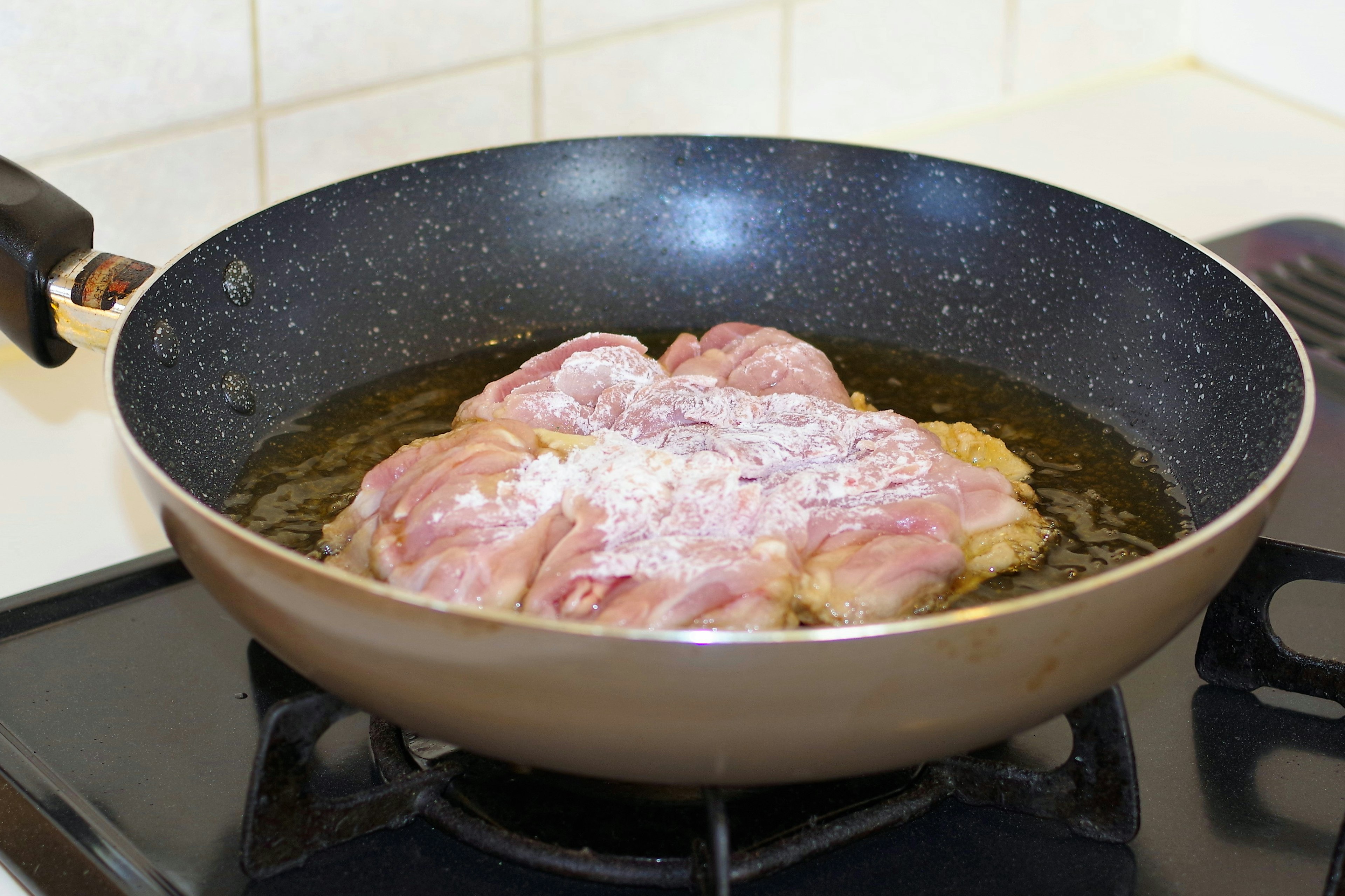 Fette di maiale che frigge in olio in una padella