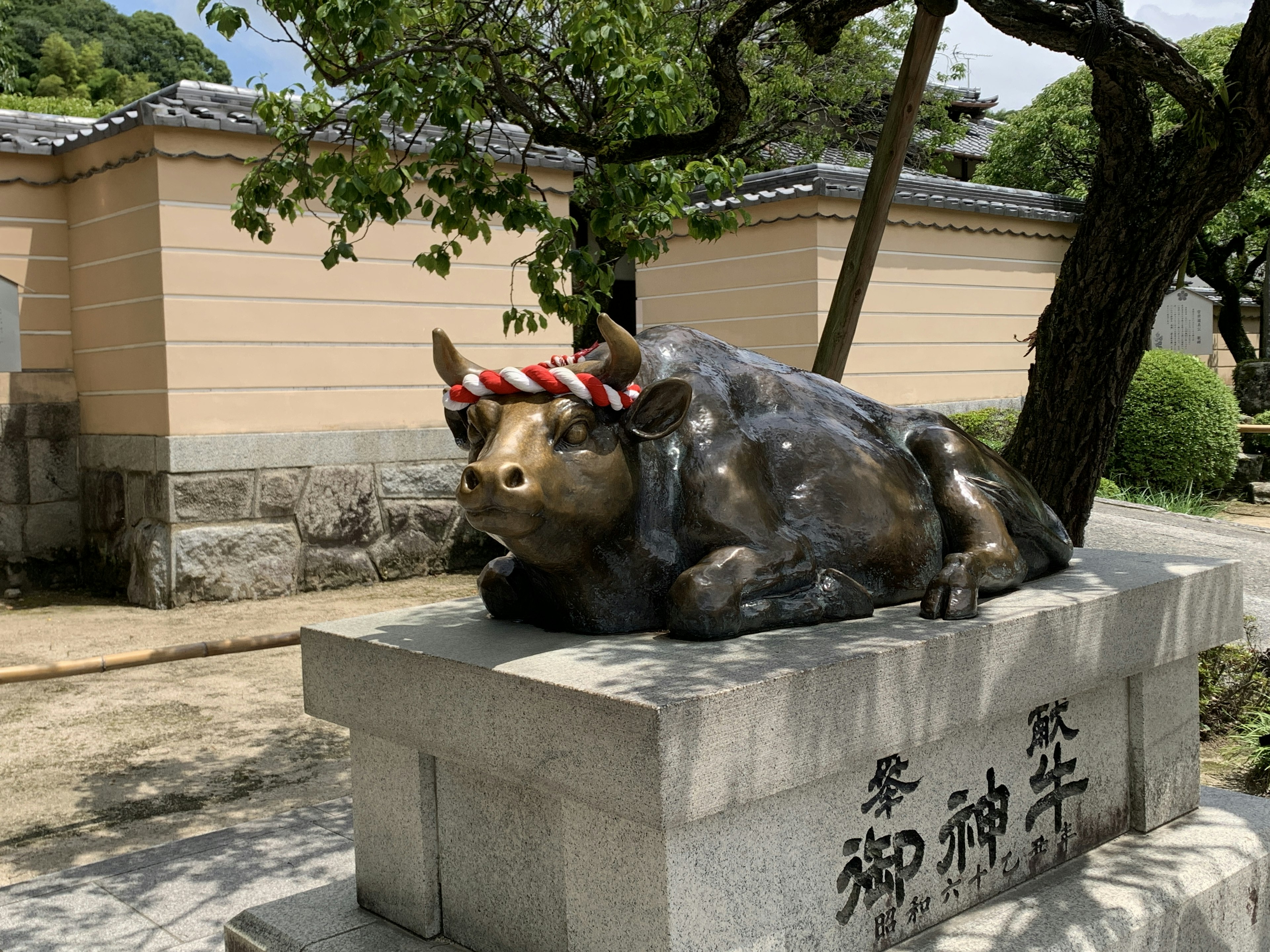 Una estatua de bronce de una vaca con una banda decorativa sobre un pedestal de piedra