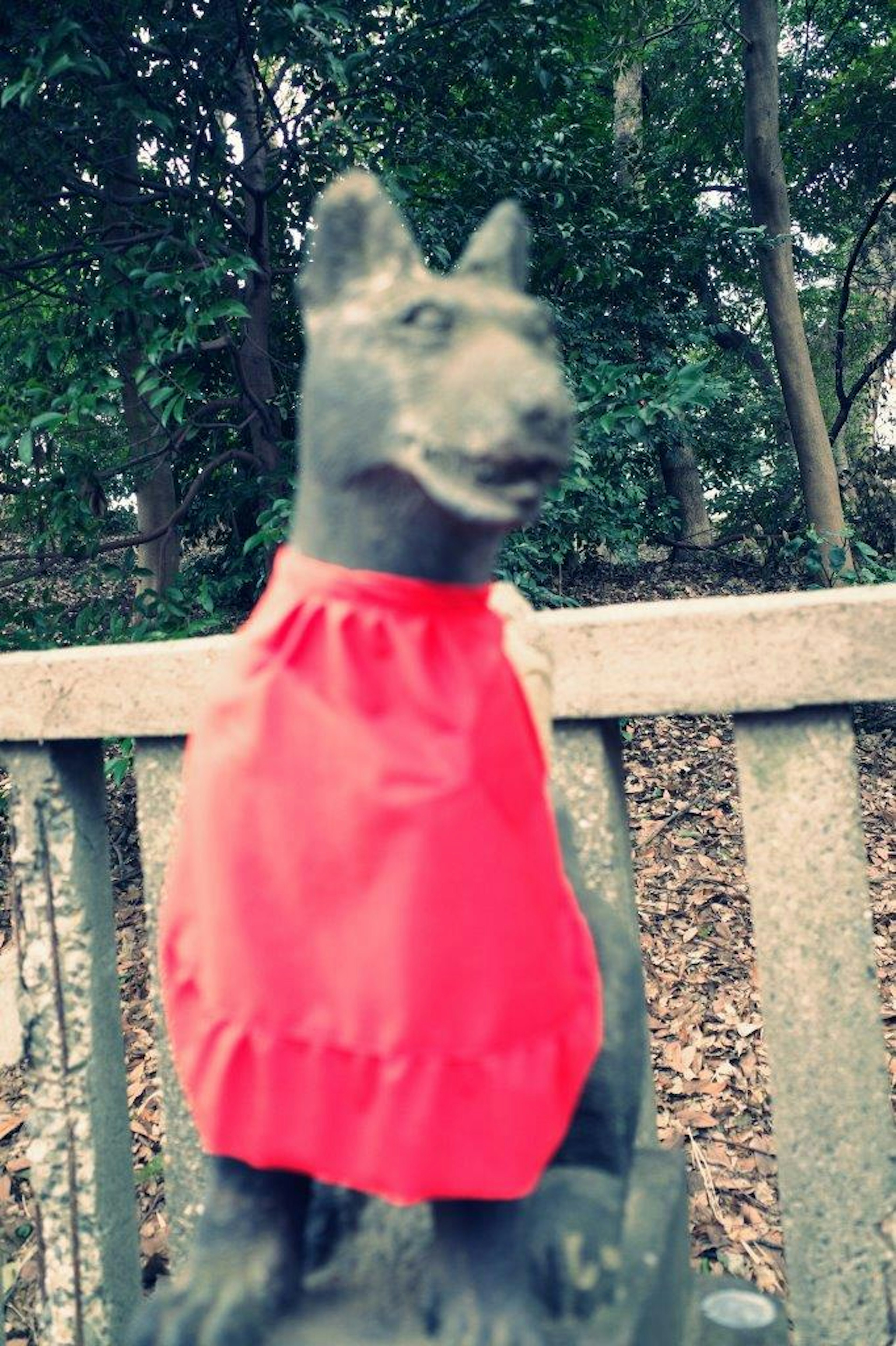 Une statue de chien portant un vêtement rouge entourée d'arbres