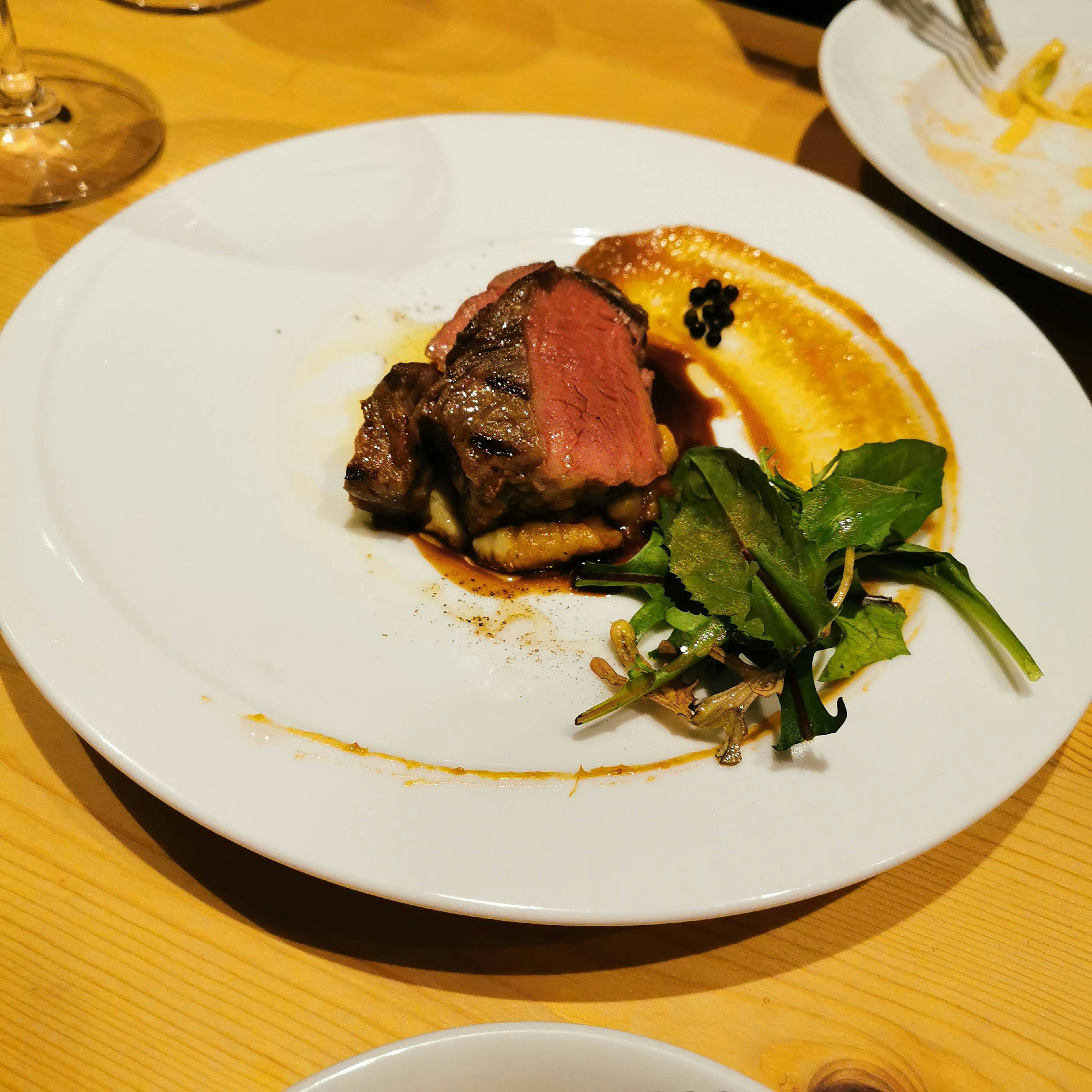 A delicious steak with a slice of sweet potato and fresh greens on a white plate