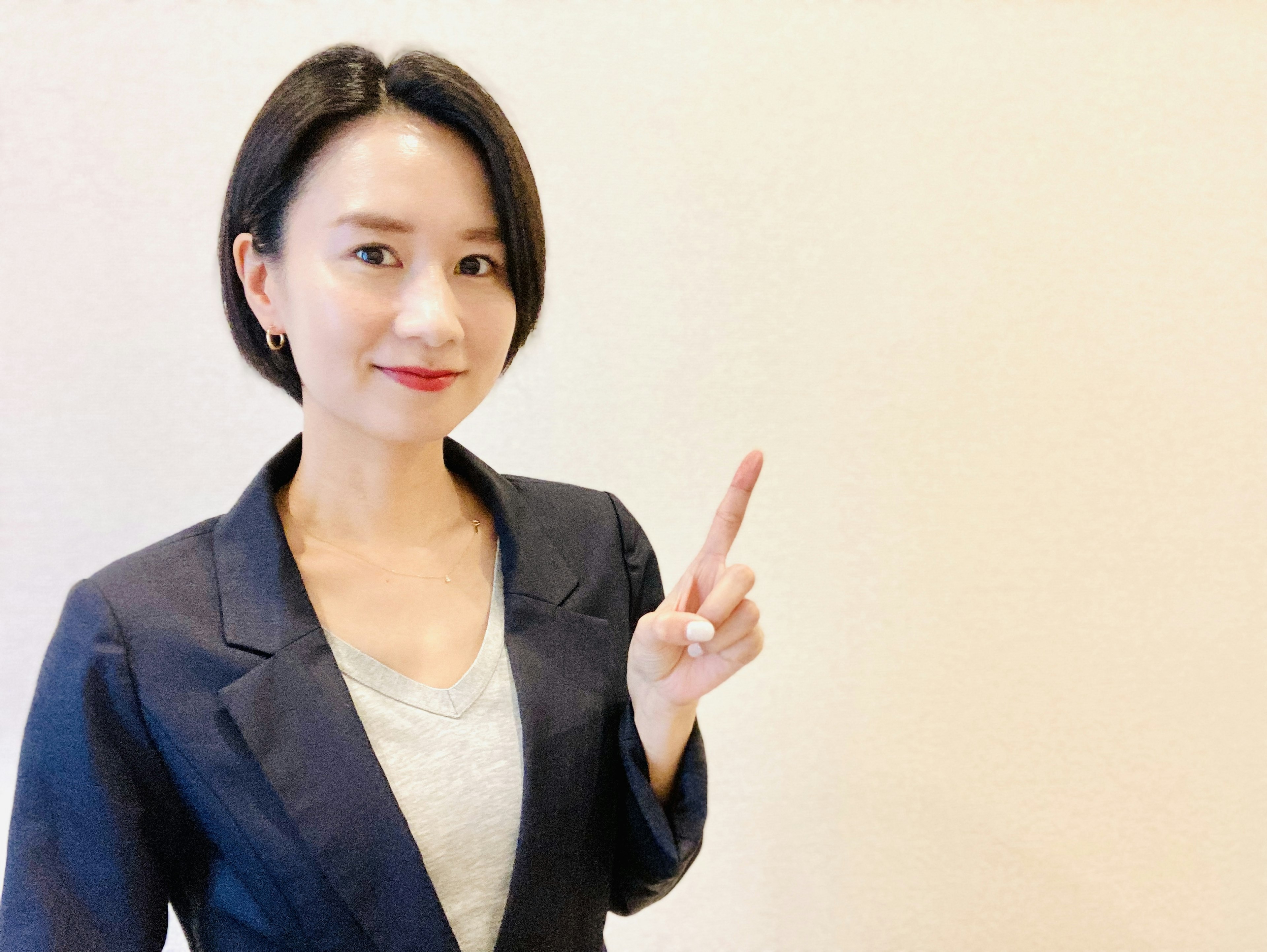 A woman in a business suit smiling and holding up her index finger