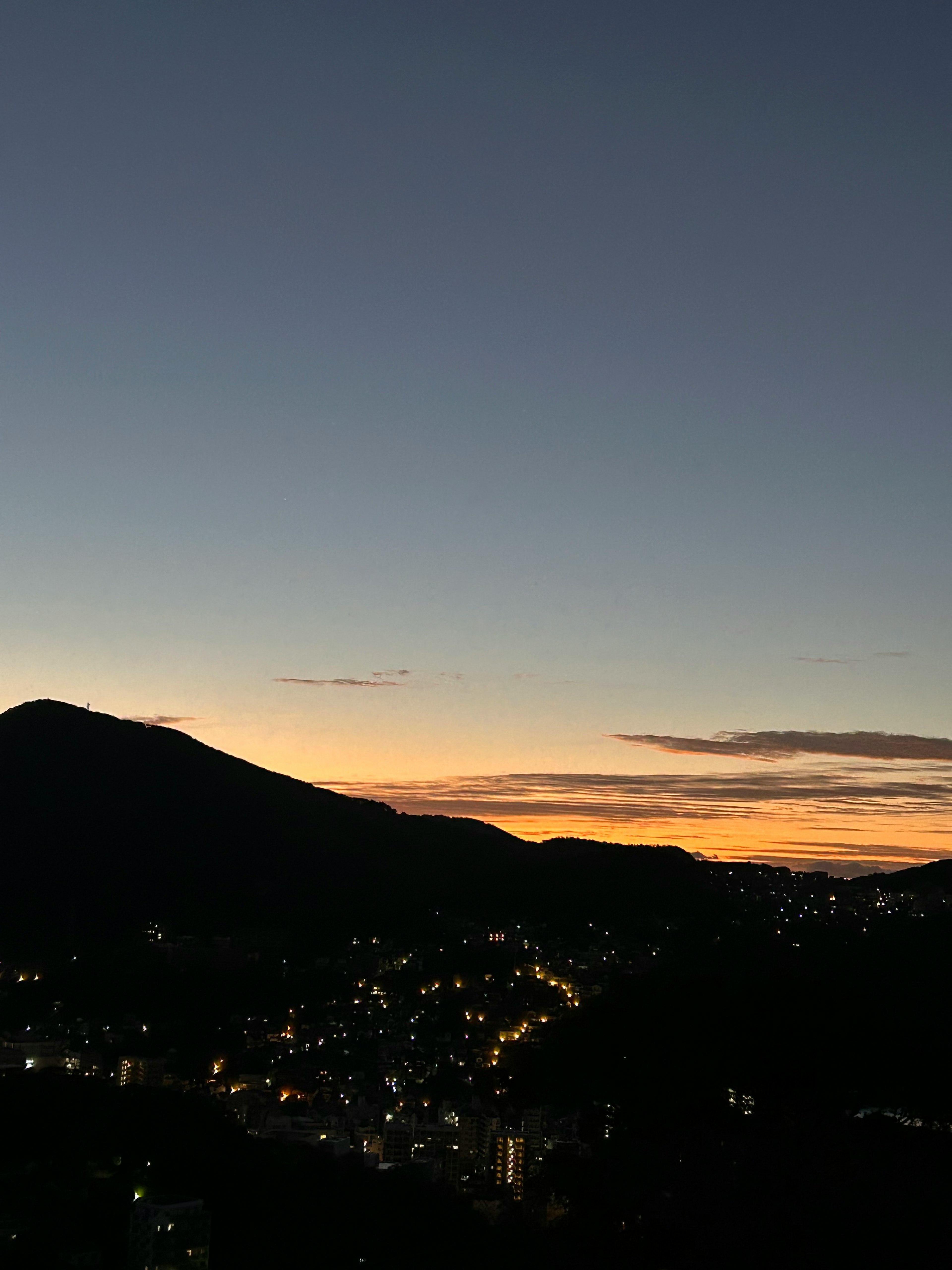 Silhouette di montagne al crepuscolo con luci di città sparse