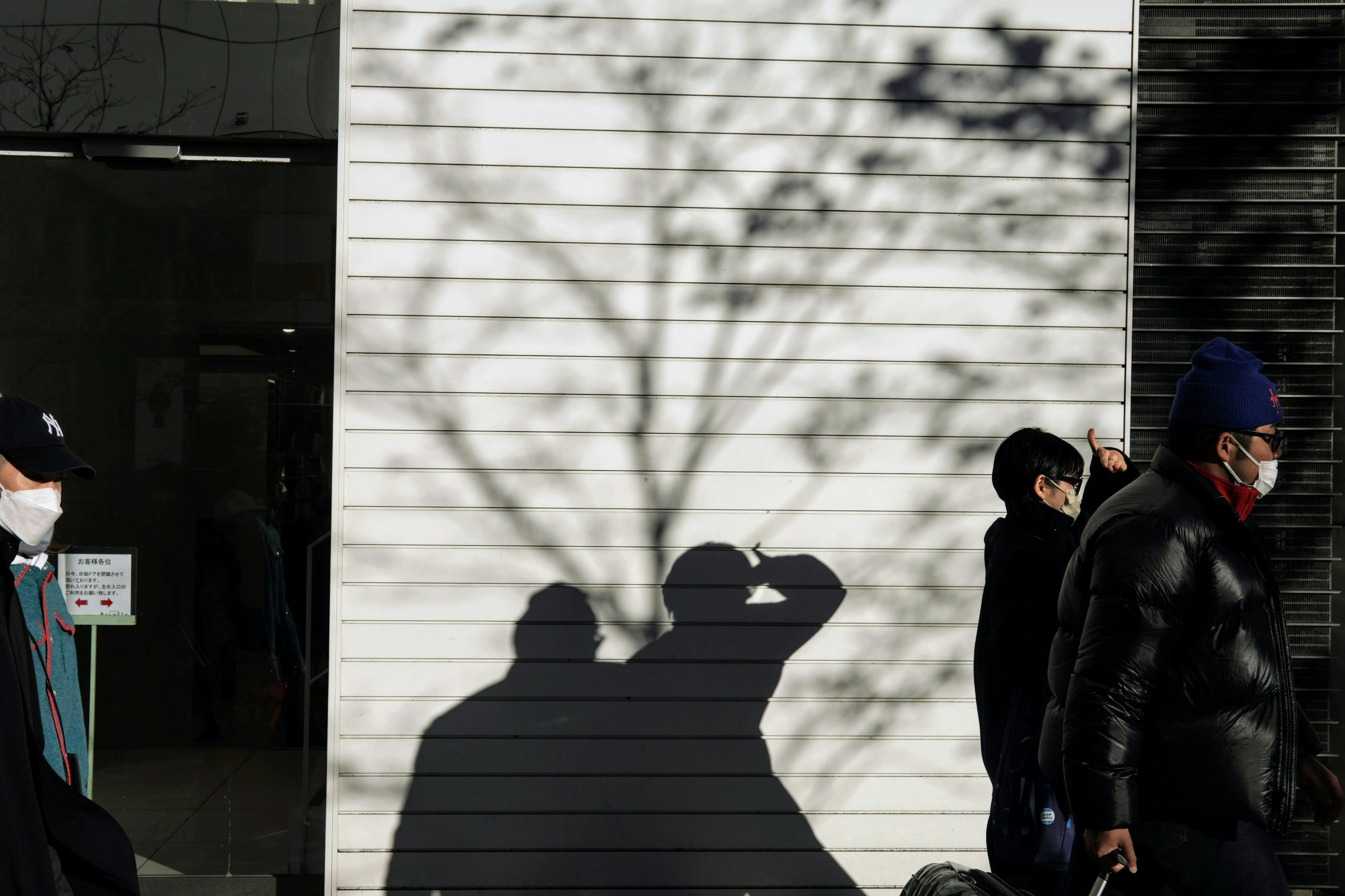 Escena urbana con sombras de personas caminando y una sombra de árbol en la pared