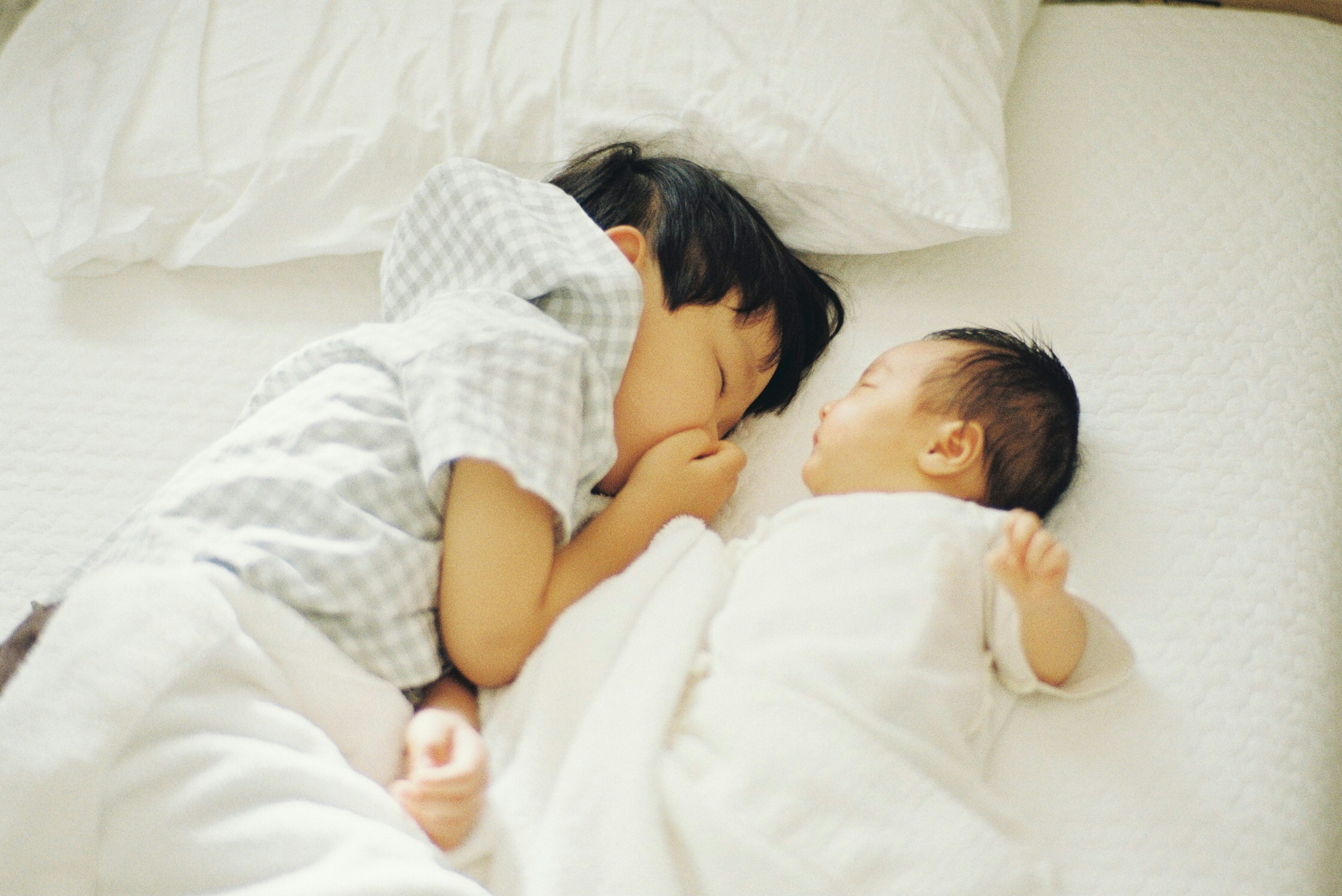 A child sleeping next to a baby on a bed