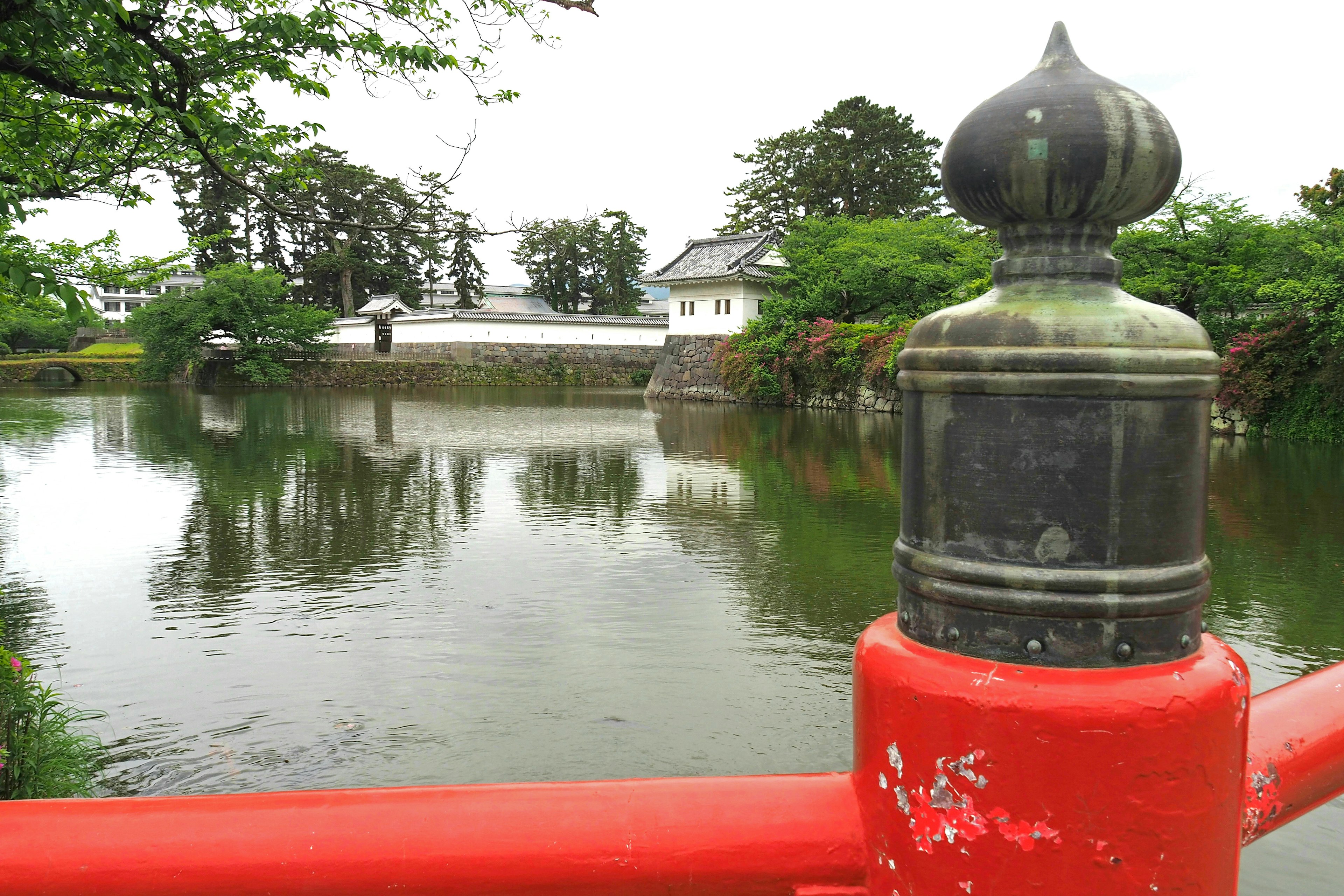 Vista de un castillo japonés con una barandilla de puente rojo y un estanque