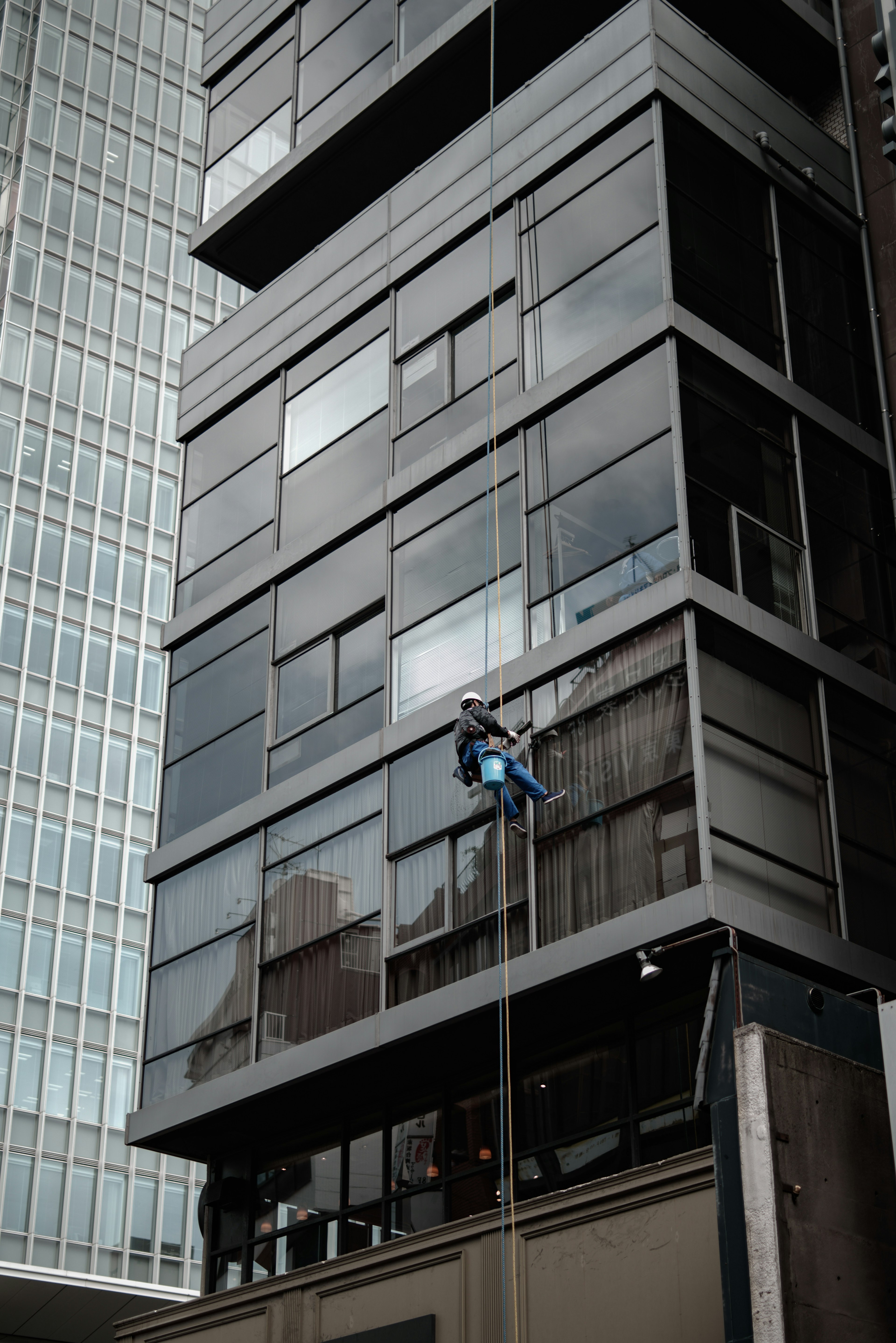 Ein Arbeiter reinigt die Fassade eines modernen Gebäudes mit großen Glasfenstern