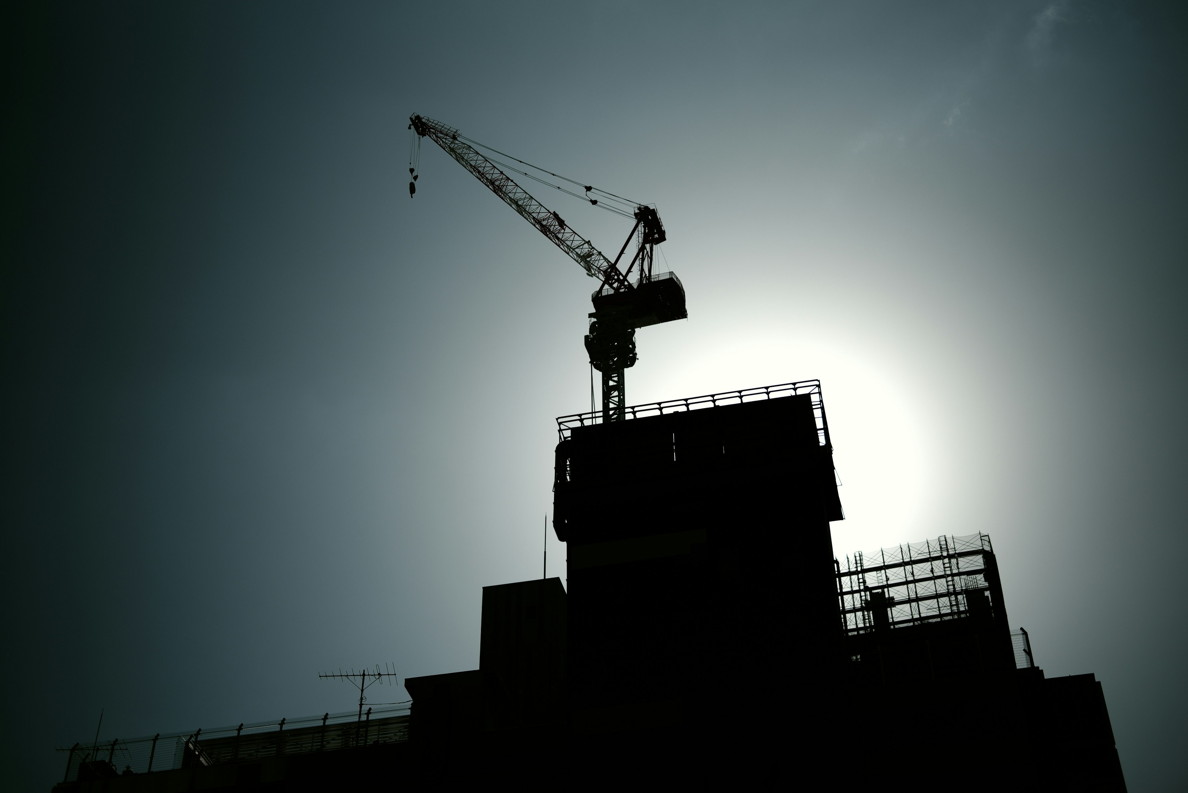 Silhouette of a construction crane atop a building under a bright sun