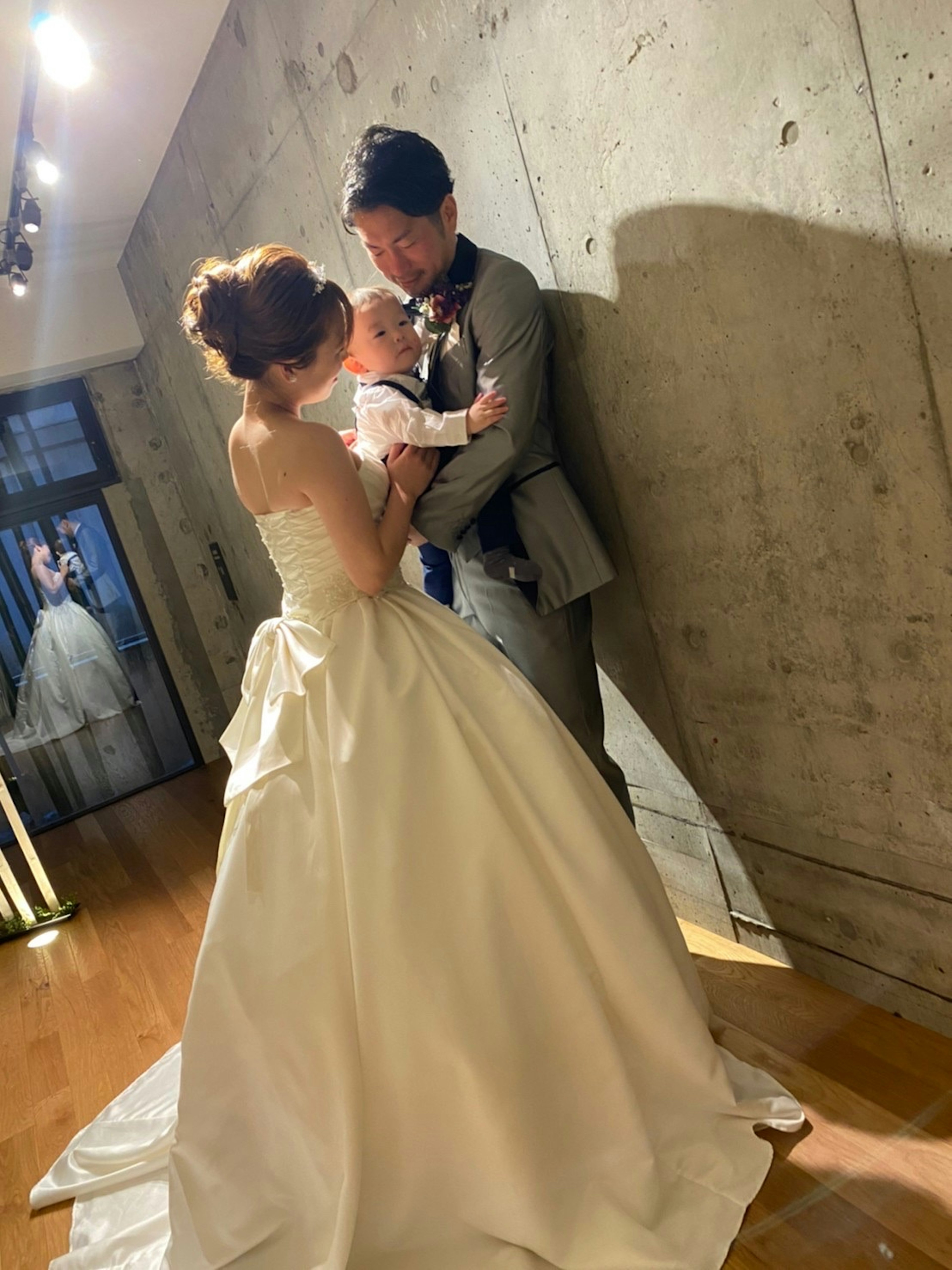 Un couple de mariés tenant un bébé dans un cadre de mariage avec une robe de mariée blanche et un costume gris