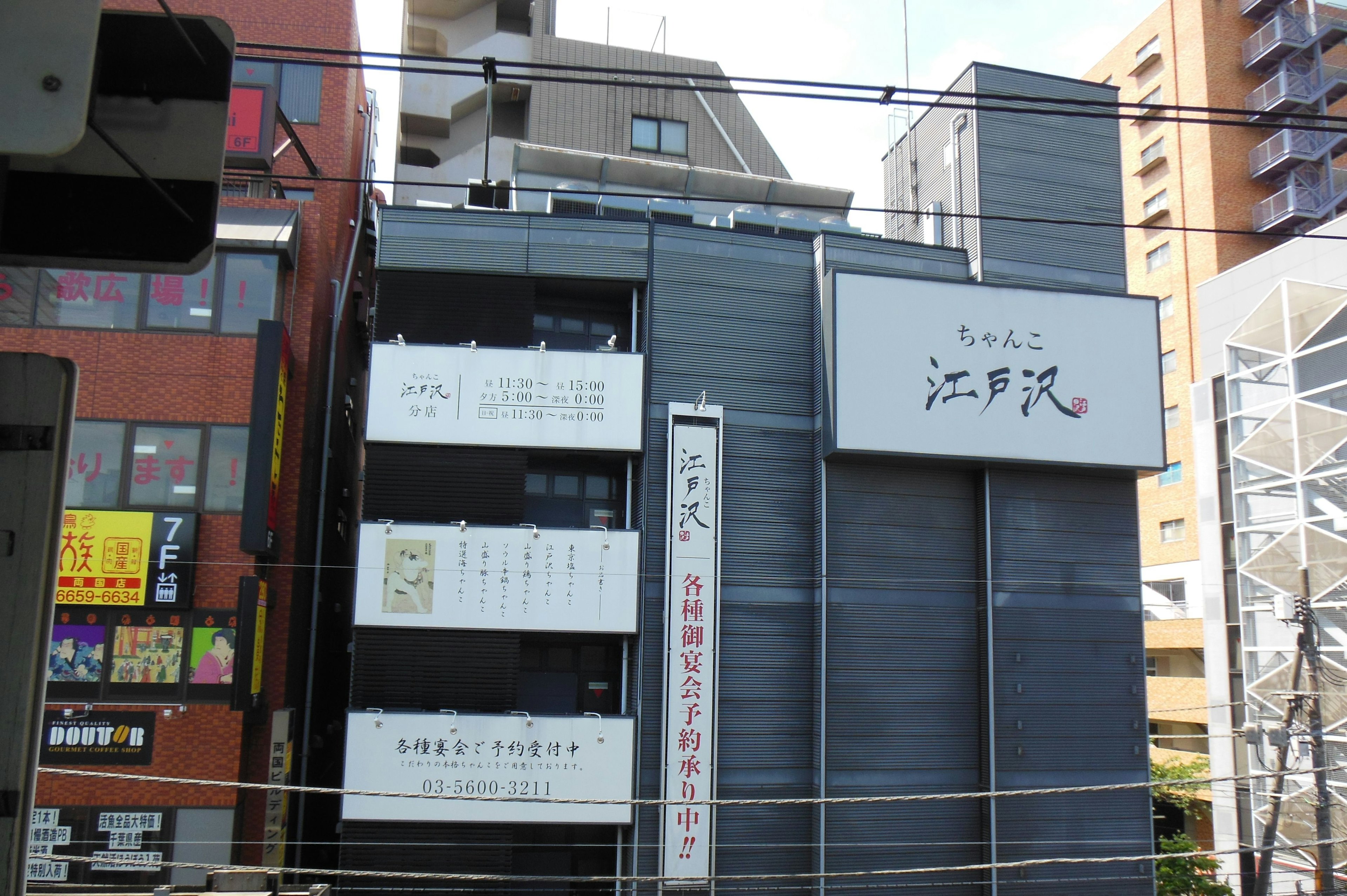 Extérieur d'un bâtiment moderne avec une enseigne en japonais entouré d'autres établissements commerciaux