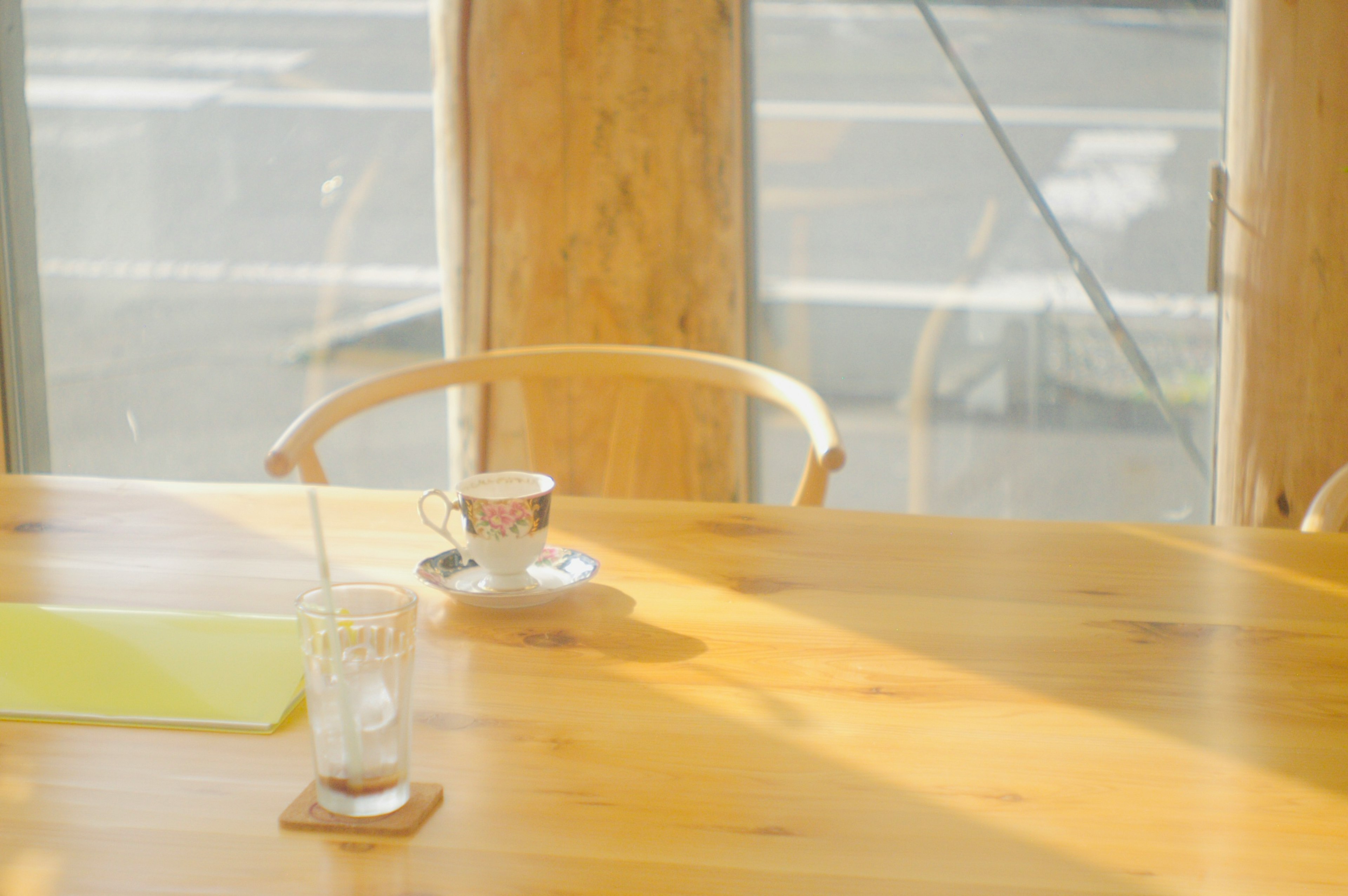 Helle Holztisch mit einer Tasse Kaffee und einem Glas Wasser Natürliches Licht strömt durch das Fenster in eine Café-Ecke