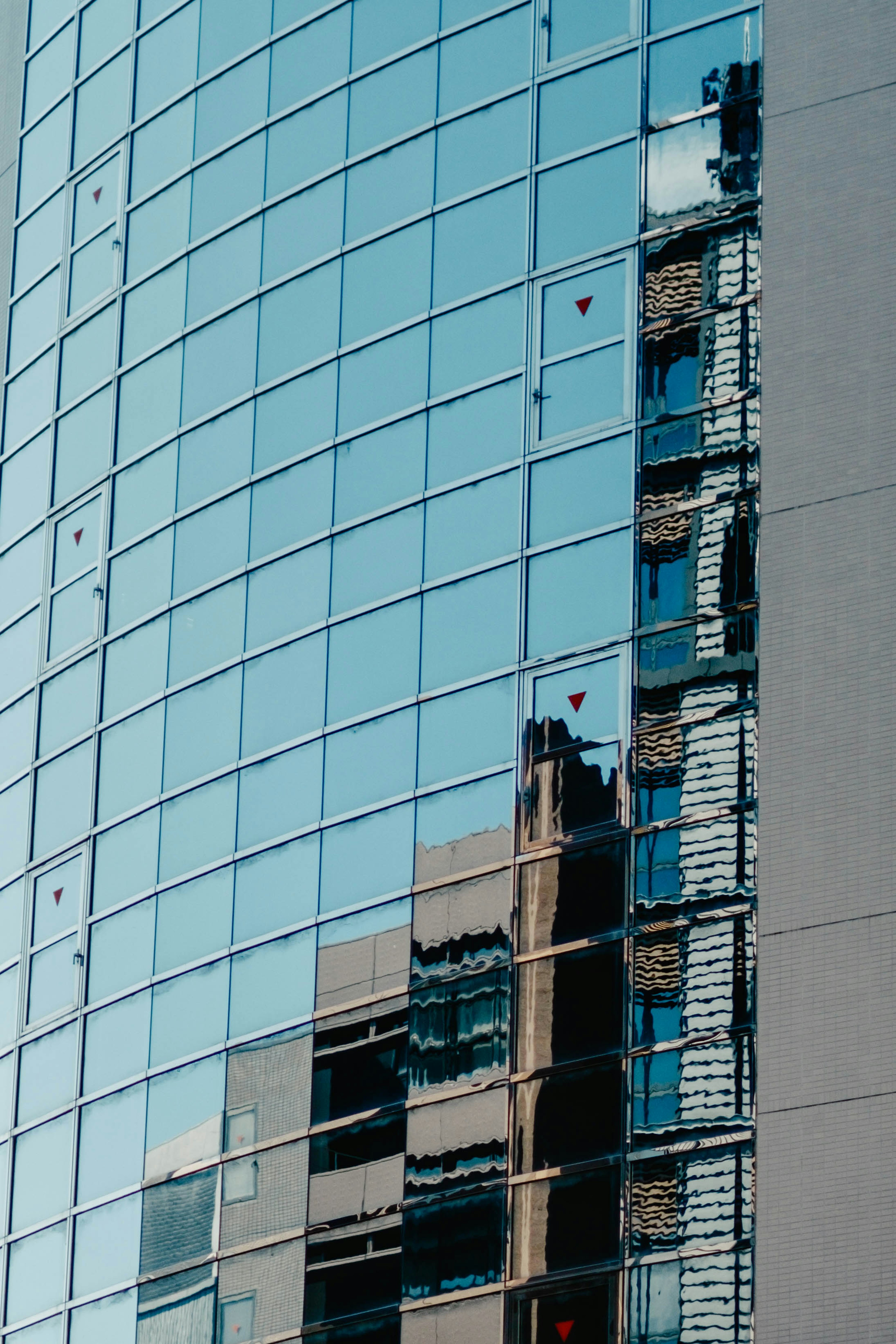 Refleksi bangunan sekitar dan langit biru di fasad kaca