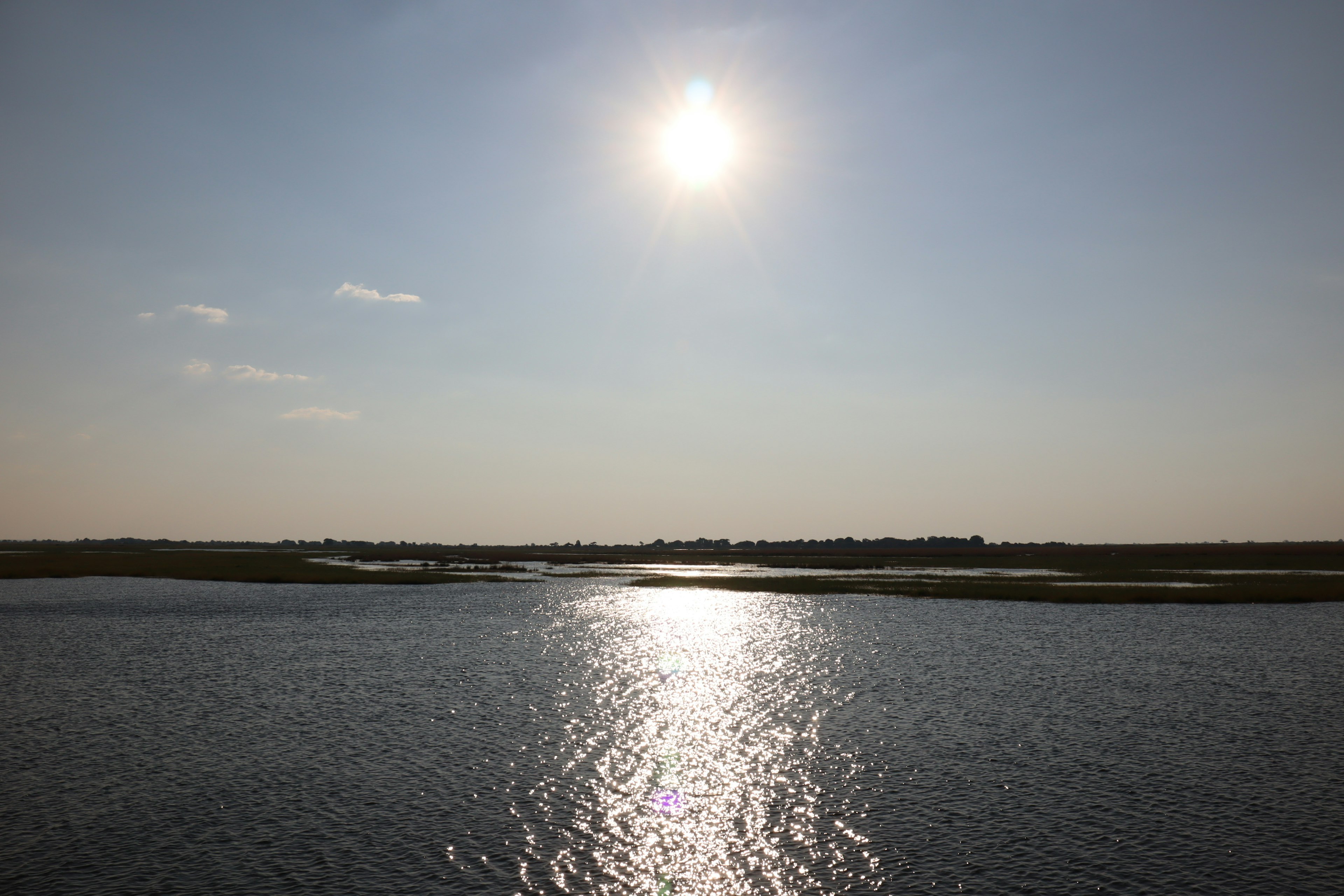 Sun reflecting on calm water with distant grassy landscape