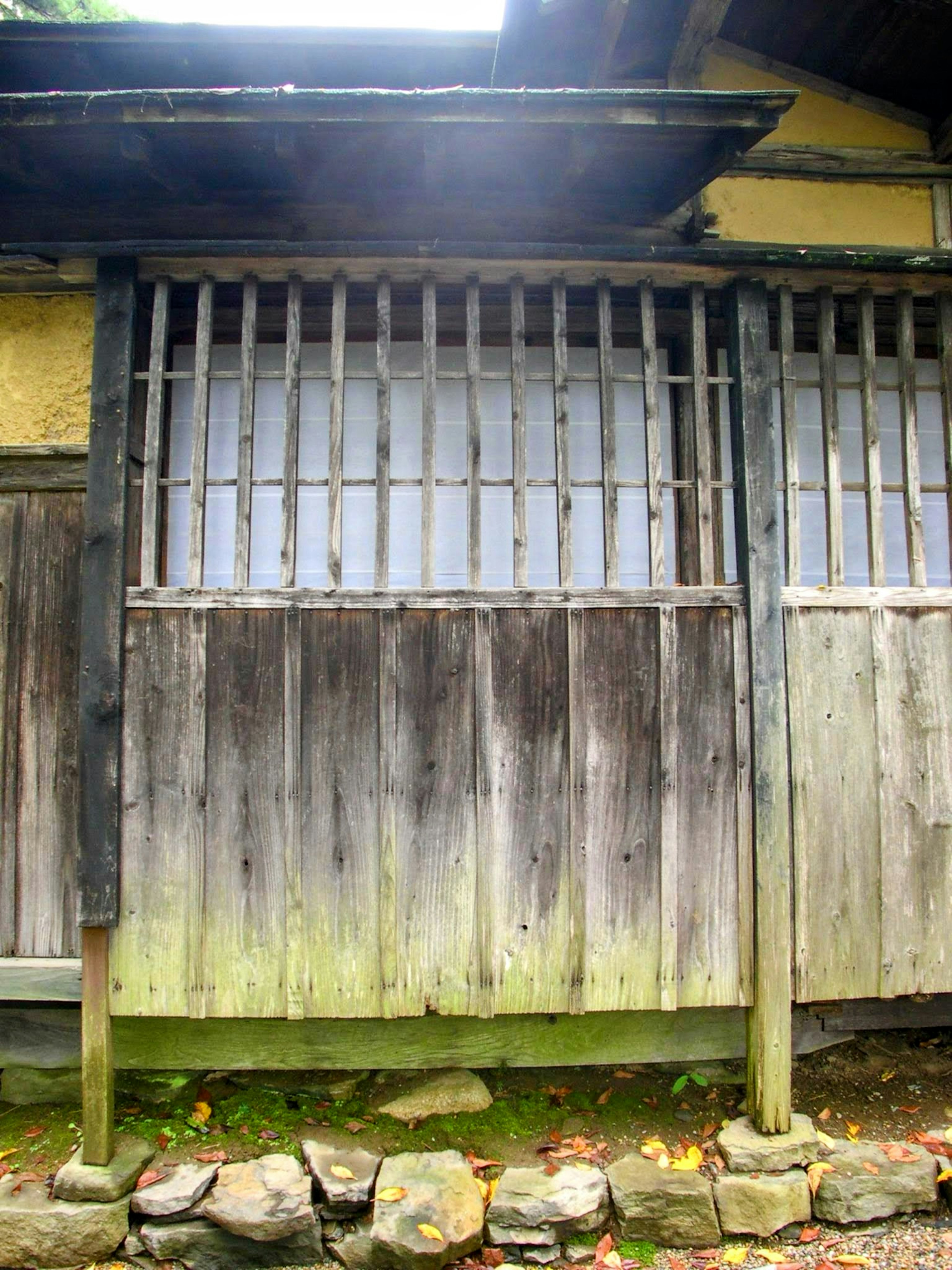 Foto de una pared de una casa de madera antigua con una ventana enrejada