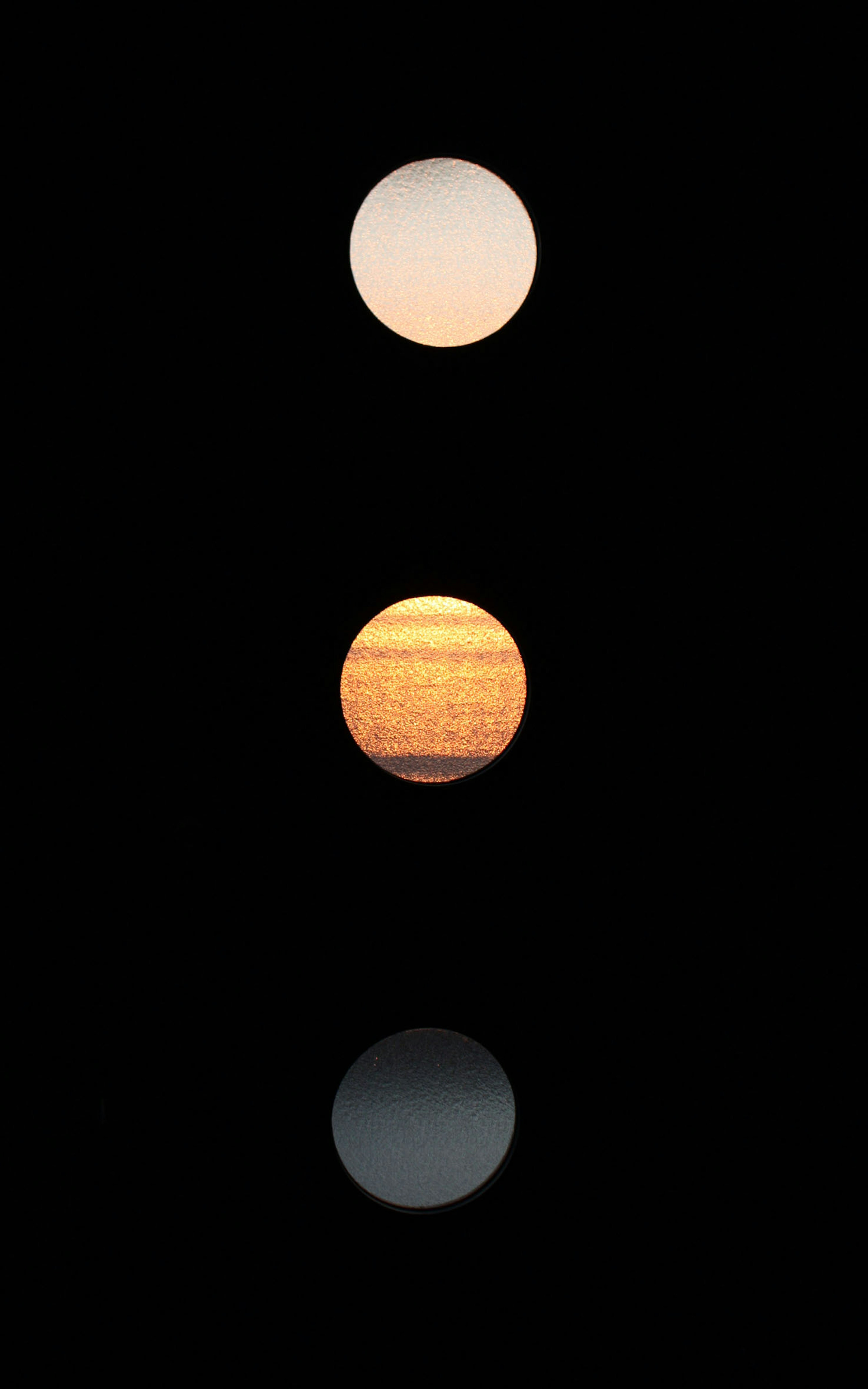 Three circular objects floating against a black background arranged vertically in light orange, orange, and dark blue