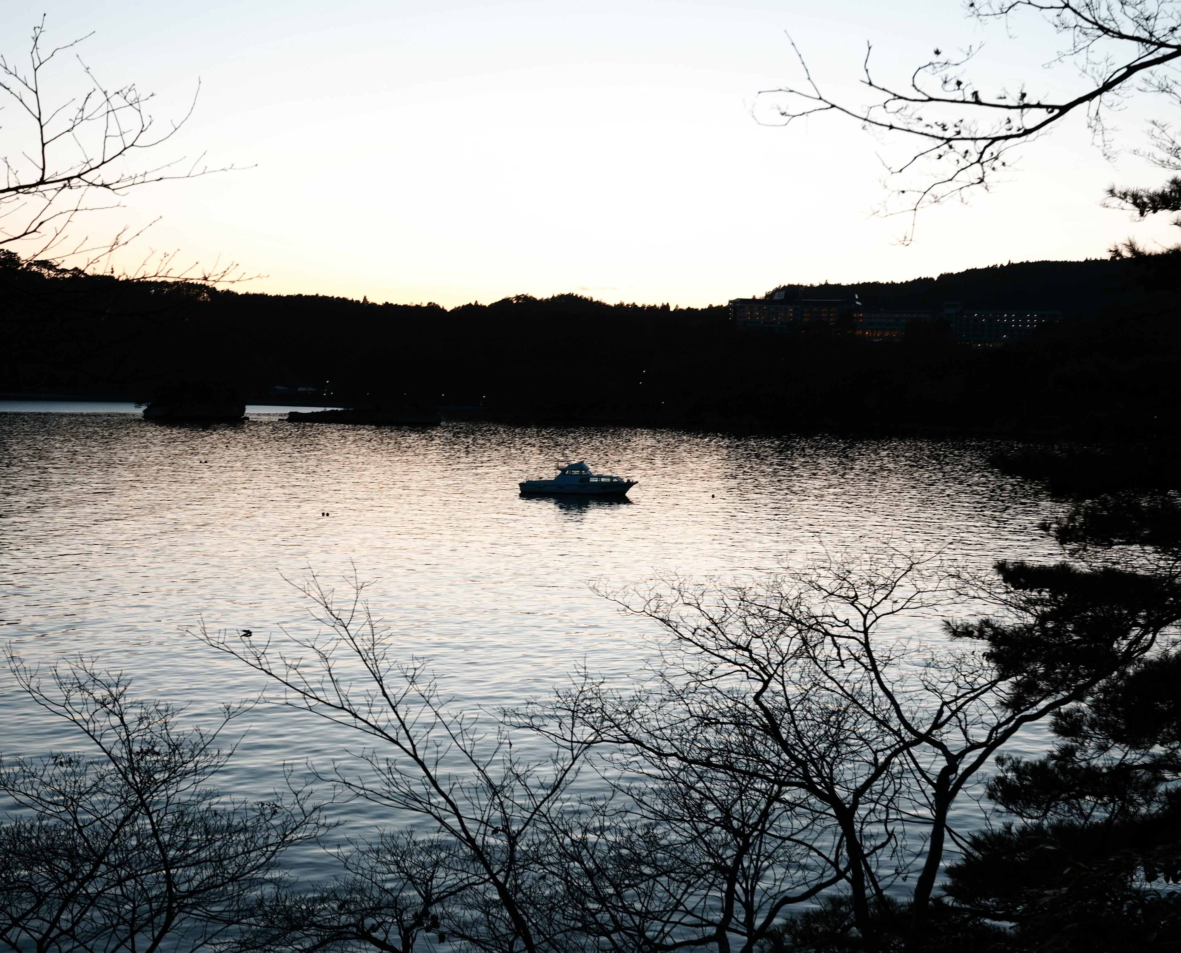 A small boat floating on a calm water surface with silhouettes of surrounding trees