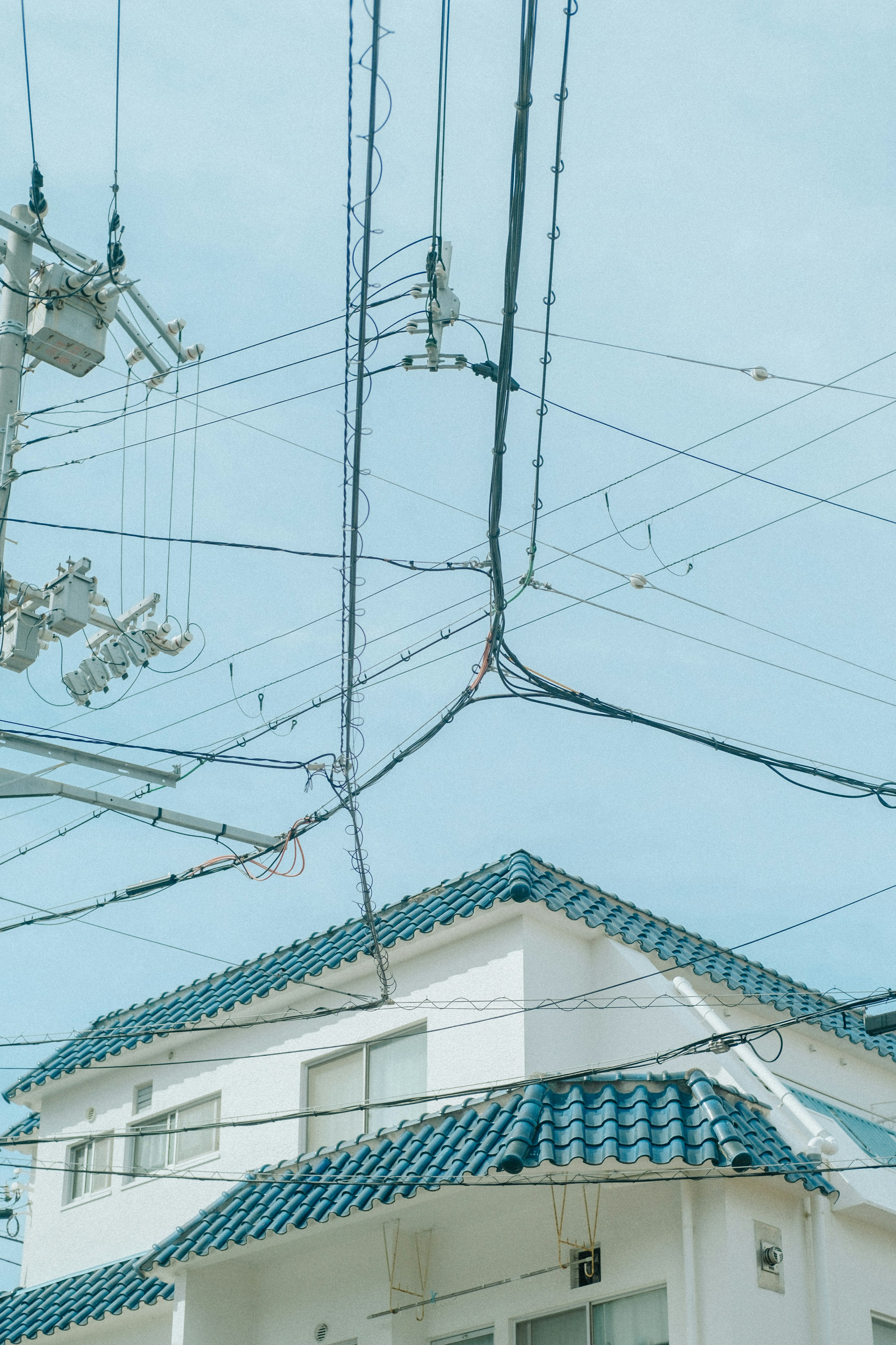 A white house with a blue roof under a clear sky with intersecting power lines