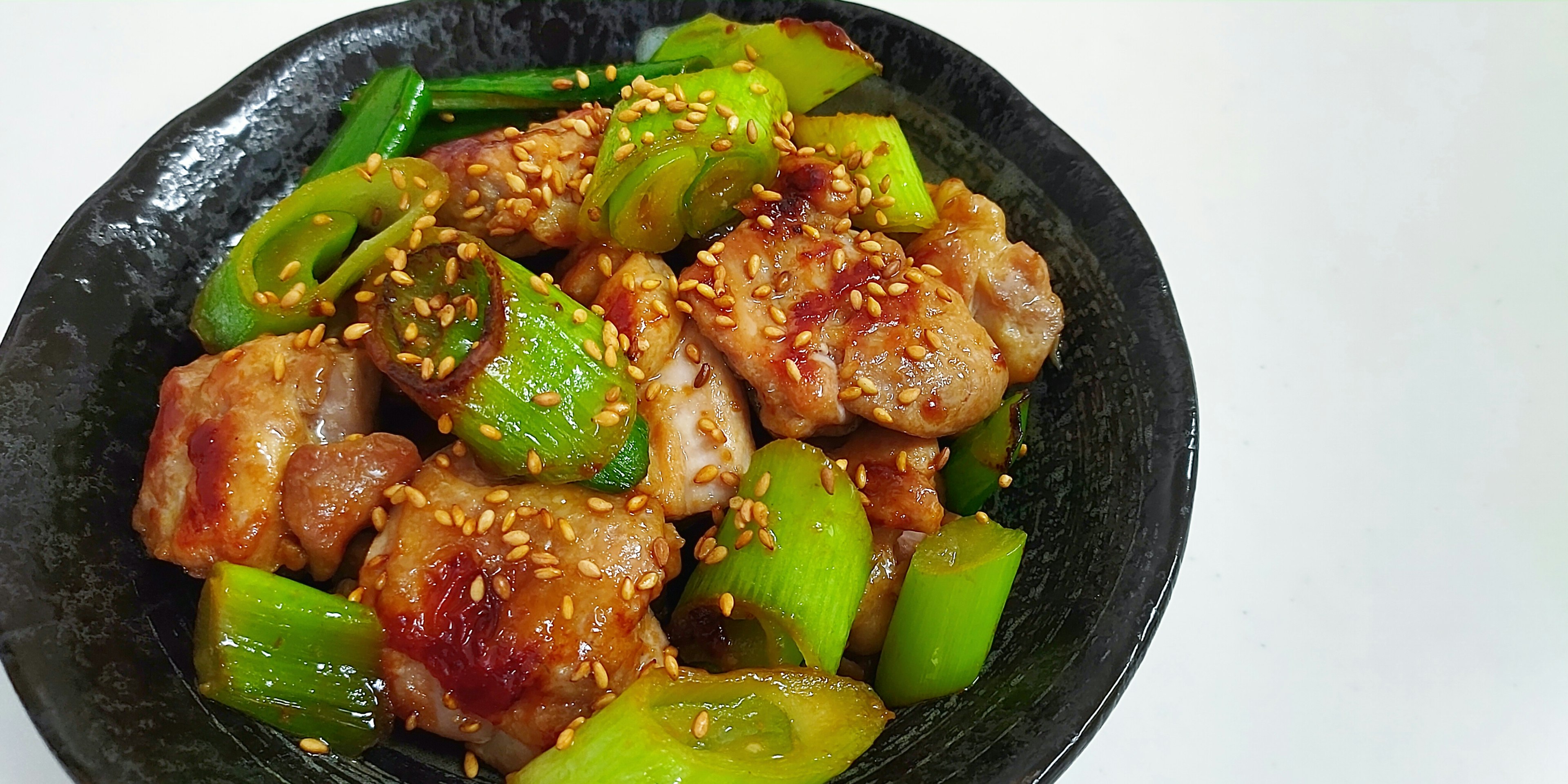 緑の野菜とセサミがトッピングされた肉料理の皿