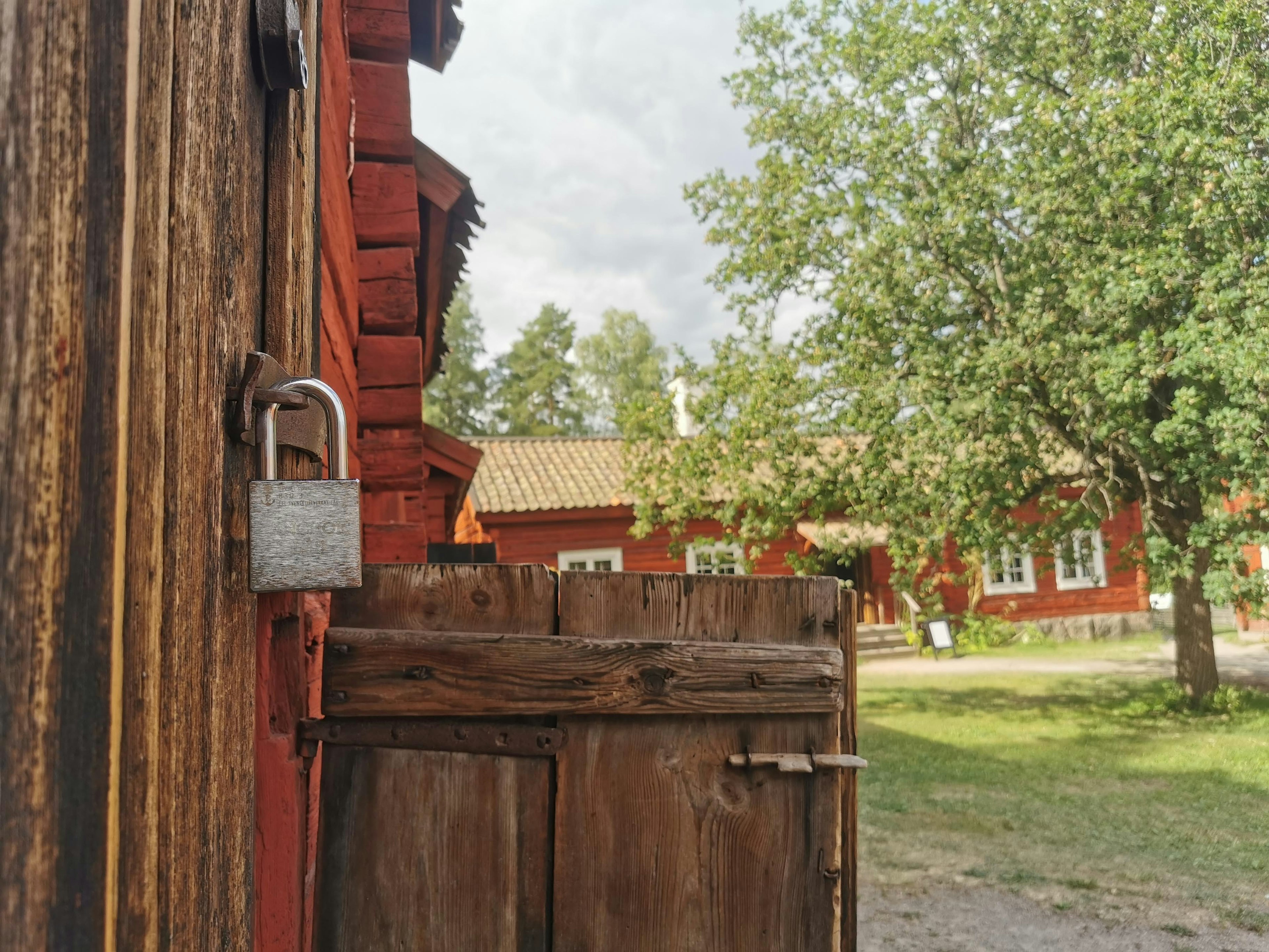 Rustikale Szene mit einer Holztür mit Vorhängeschloss und roten Gebäuden im Hintergrund