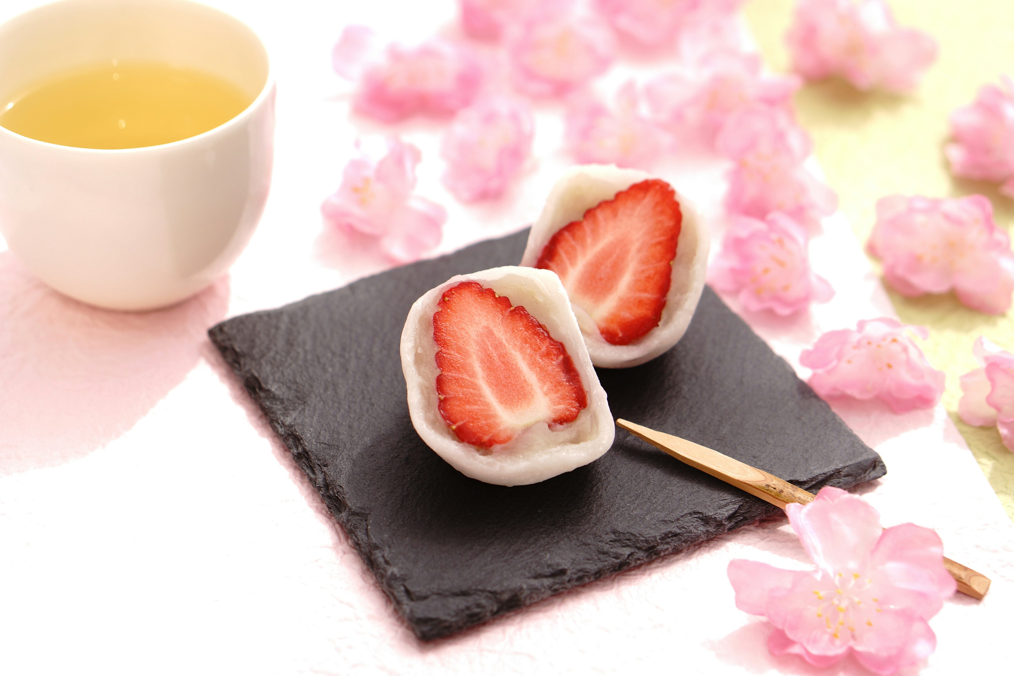 Beautifully arranged strawberry daifuku on a black slate with green tea and cherry blossoms