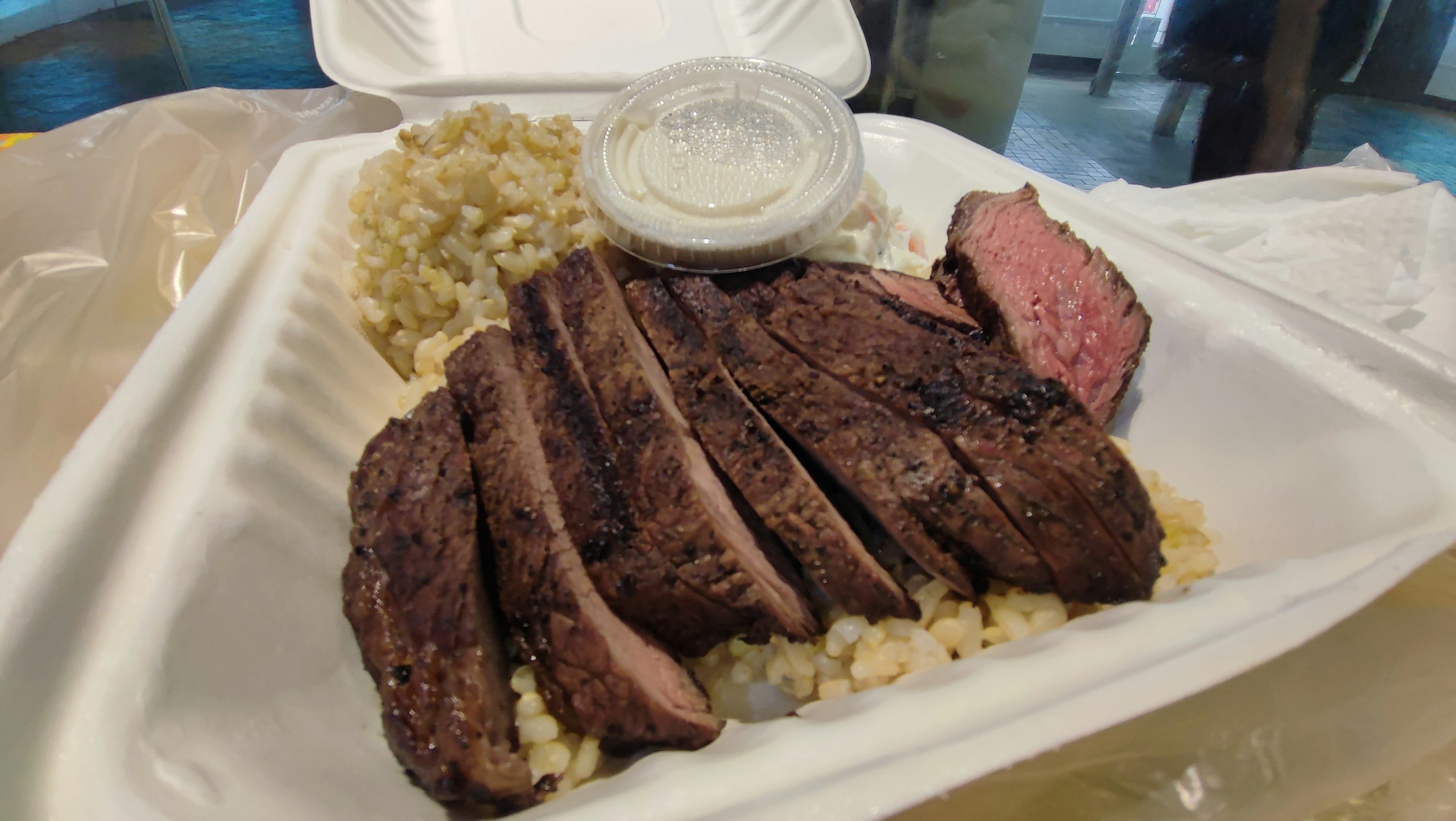 Viande grillée tranchée servie dans un conteneur blanc avec du riz et de la sauce